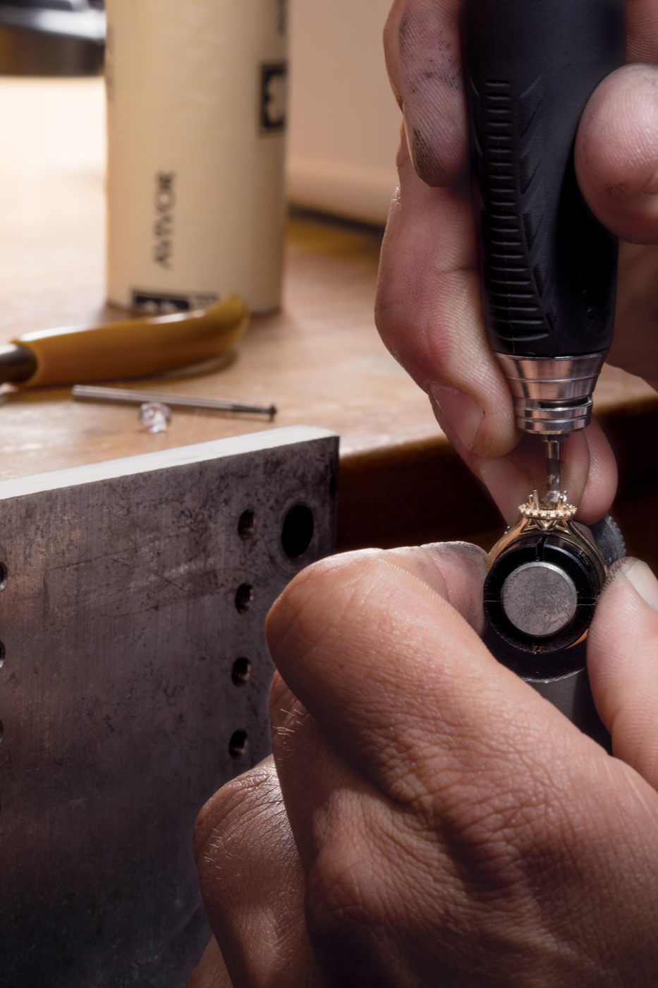 Bench jeweler using a hand tool to cut seats in prongs for a center stone.
