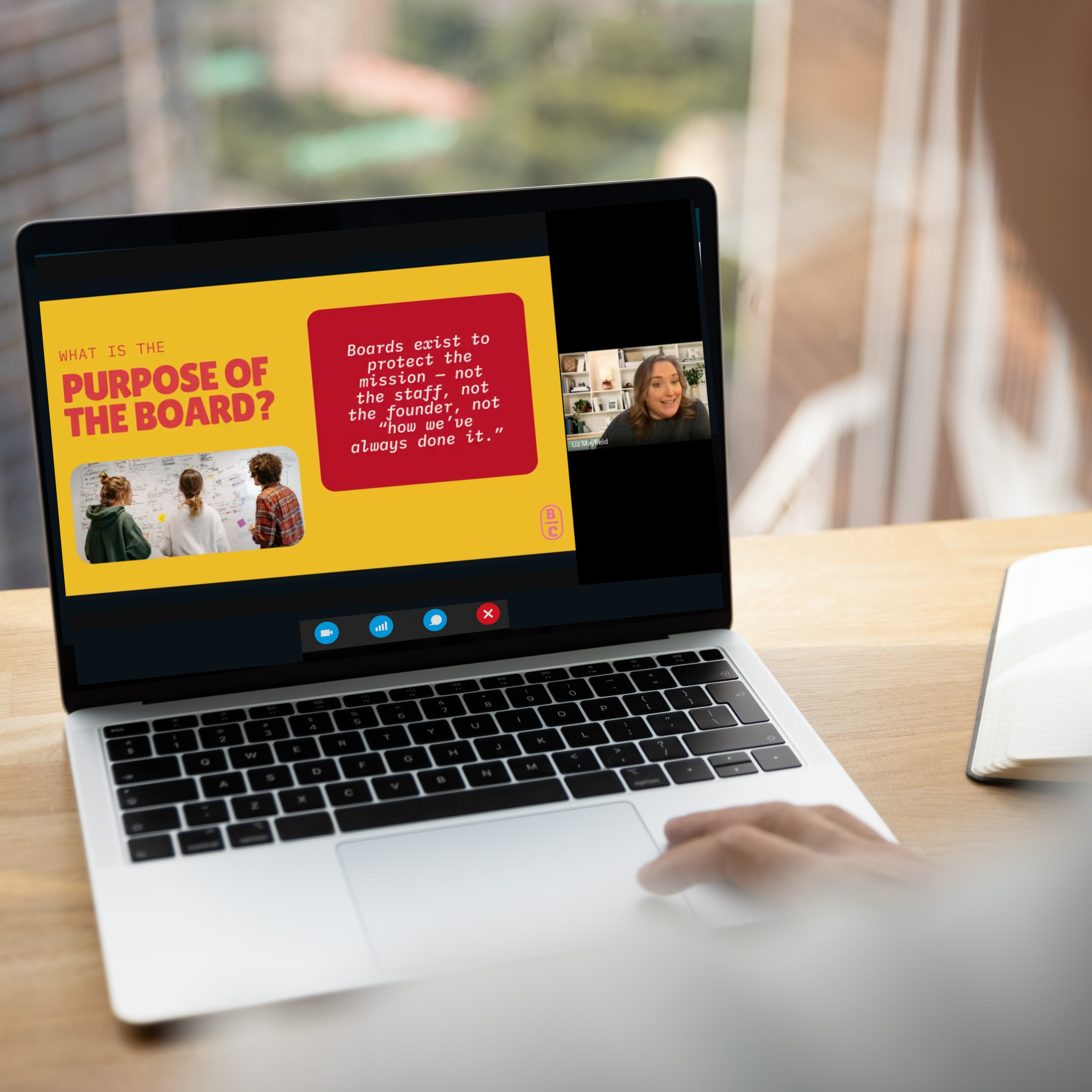 Laptop screen showing a presentation slide with the title "What is the Purpose of the Board?" and a quote about boards. There is a video call window with a woman speaking, and the laptop is on a wooden desk with a notebook nearby.