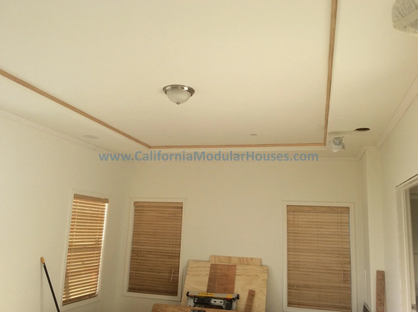 Room under construction with plywood on walls, construction tools, and window blinds.