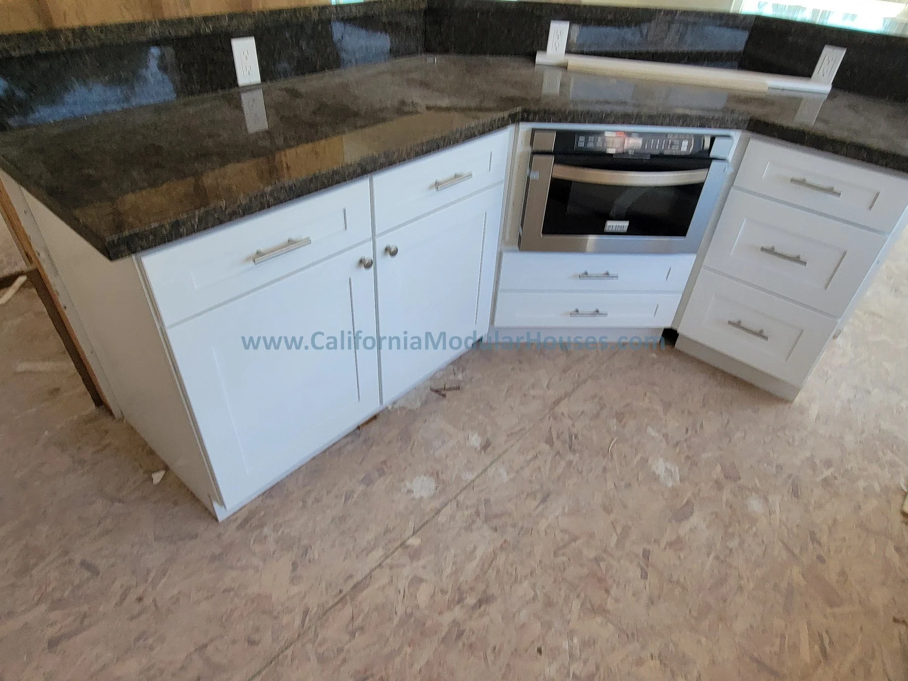 Kitchen corner with white cabinets, dark granite countertop, and built-in microwave oven, with electrical outlets on the backsplash.