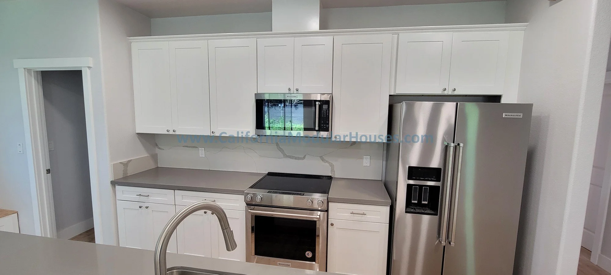 Modern kitchen with stainless steel refrigerator with water and ice dispenser, stainless steel oven, microwave, white cabinets, and grey countertops.
