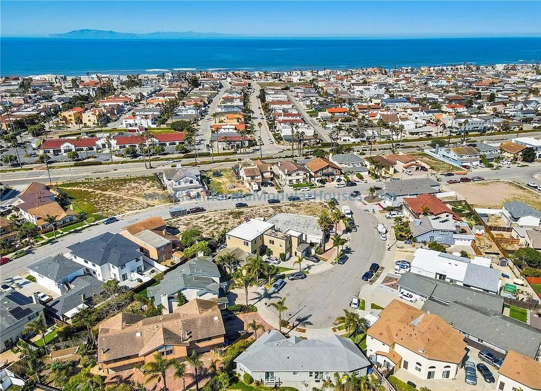 Aerial view of a coastal residential neighborhood with houses, streets, palm trees, and the ocean in the background.   California Modular Houses. Modular home construction California.  Prefab house.  Oxnard, Ventura County, CA.  