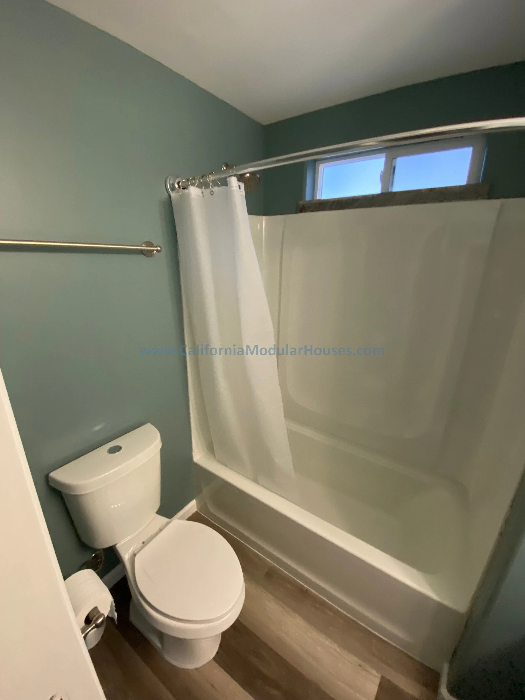 Interior bathroom with a toilet, bathtub with a shower curtain, and a small window above the bathtub.   Modular ADU  Modular Contra Costa County, CA.  