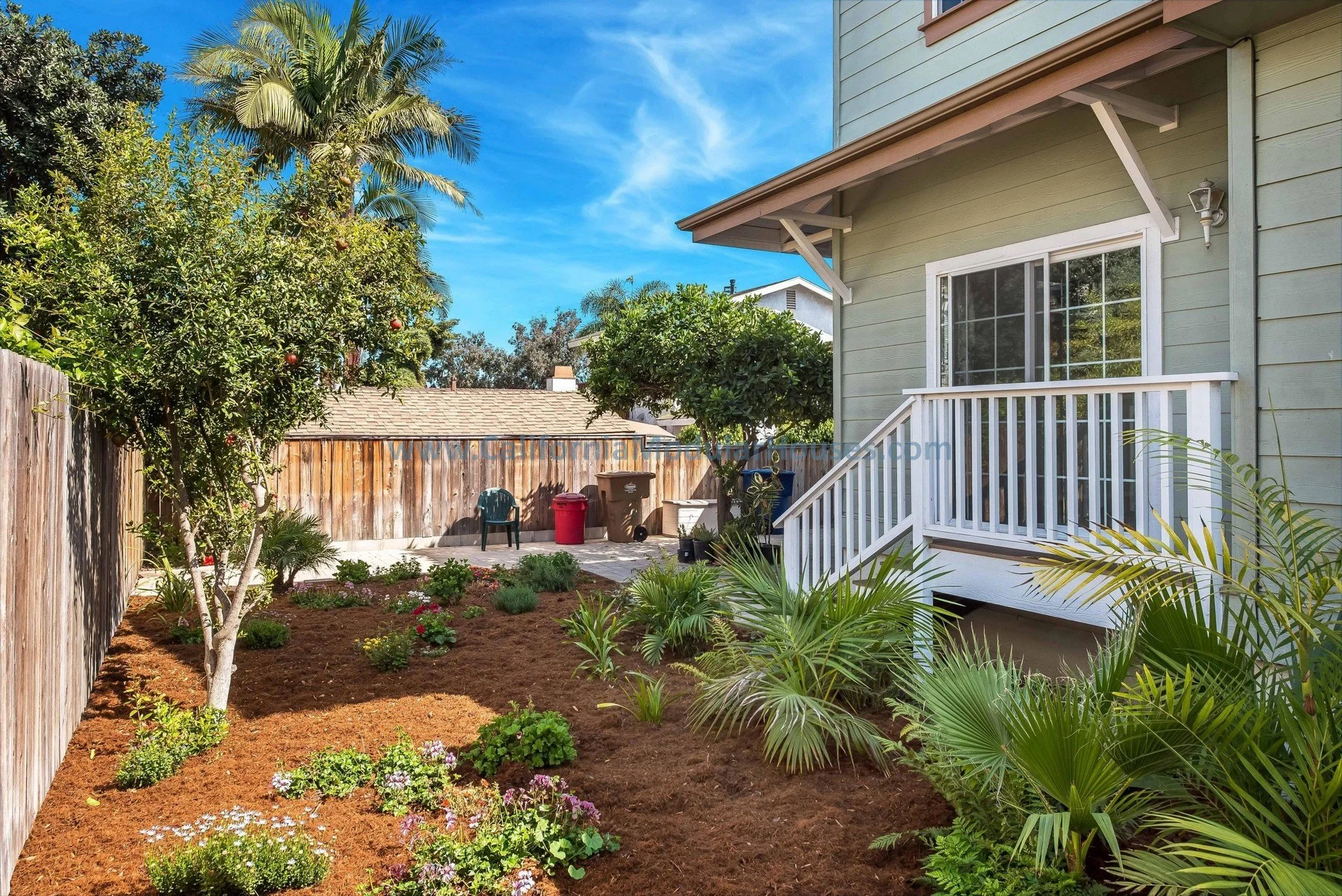 Backyard view of a sage green, brown trim prefab modular, two-story home. White door, white railing.