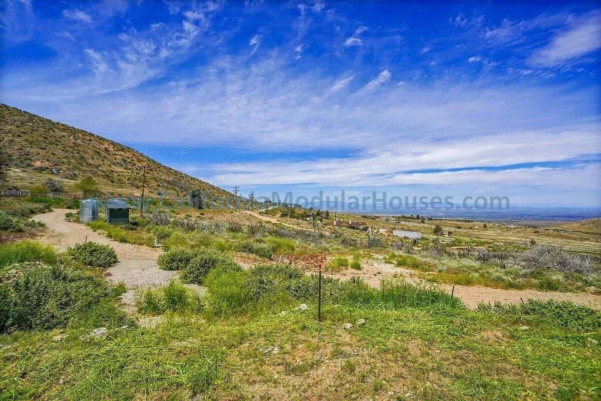 Open landscape with hills, green shrubs, and a partly cloudy blue sky.