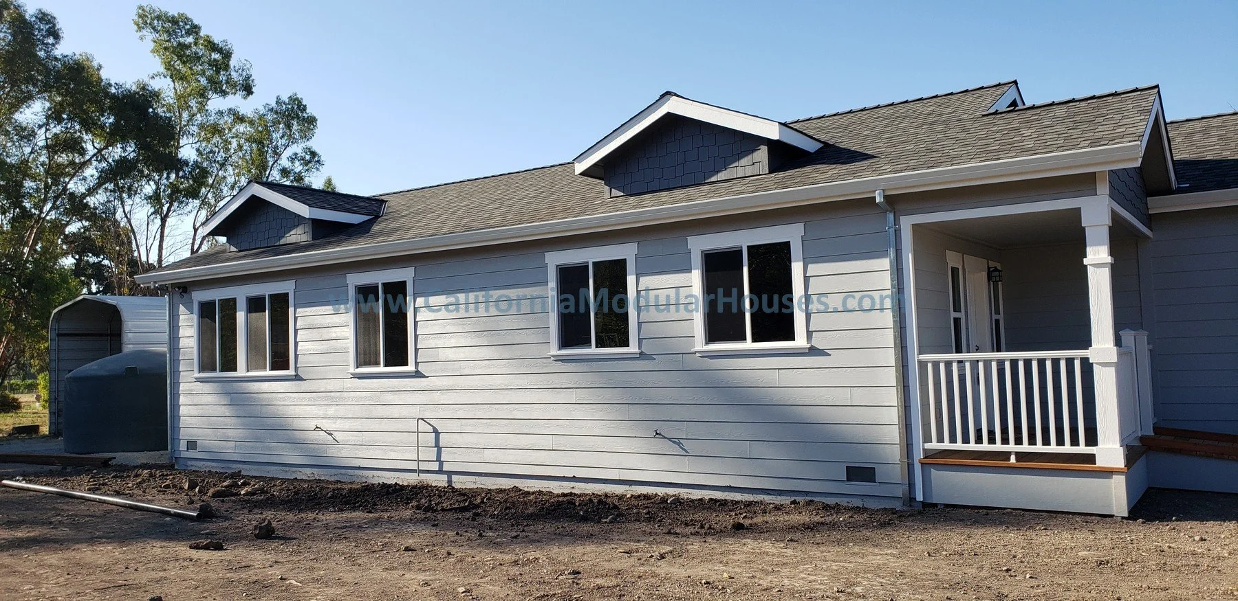 Side view of a newly built house with white horizontal siding, black shingle roof, multiple windows, a small porch with white railings.  Modular granny flat.  California.   Kenwood, Sonoma County, CA. 