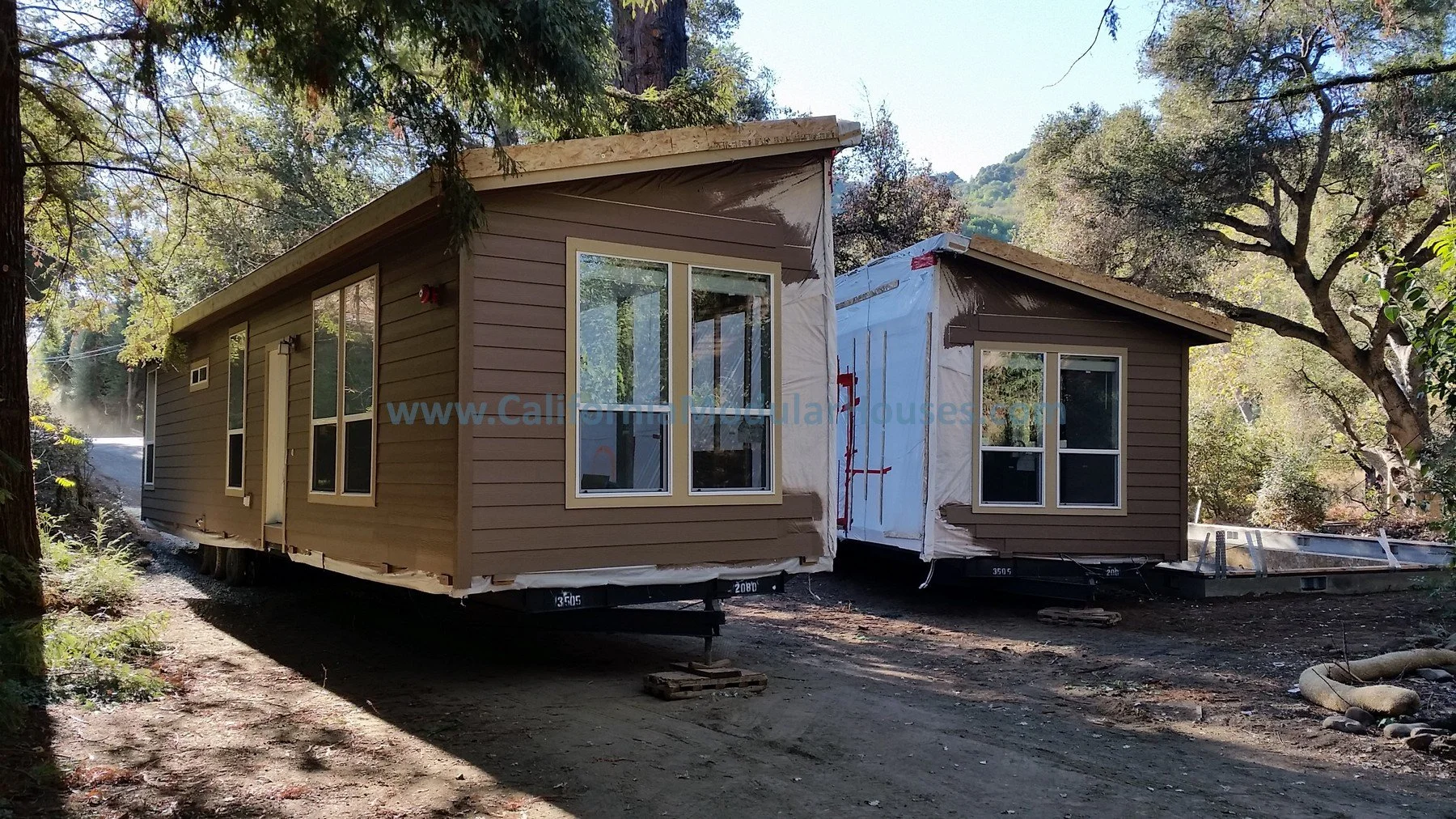 Modular sections being delivered for construction with one fully completed and the other still wrapped in protective plastic, surrounded by trees and natural landscape.   Modular granny flat.  California.   