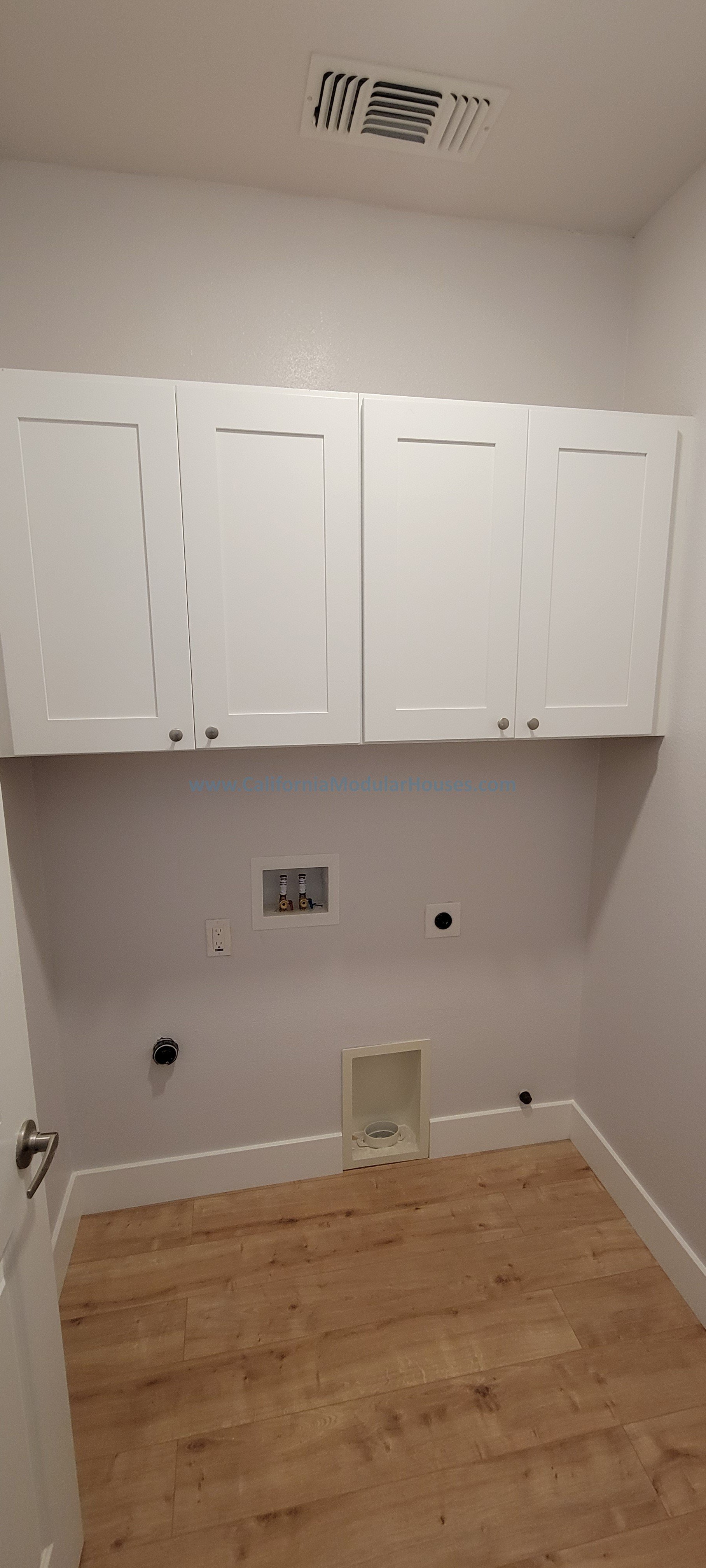 Empty laundry room with white cabinets, a vent on the ceiling, and hookups for washer and dryer on the wall, with hardwood flooring.