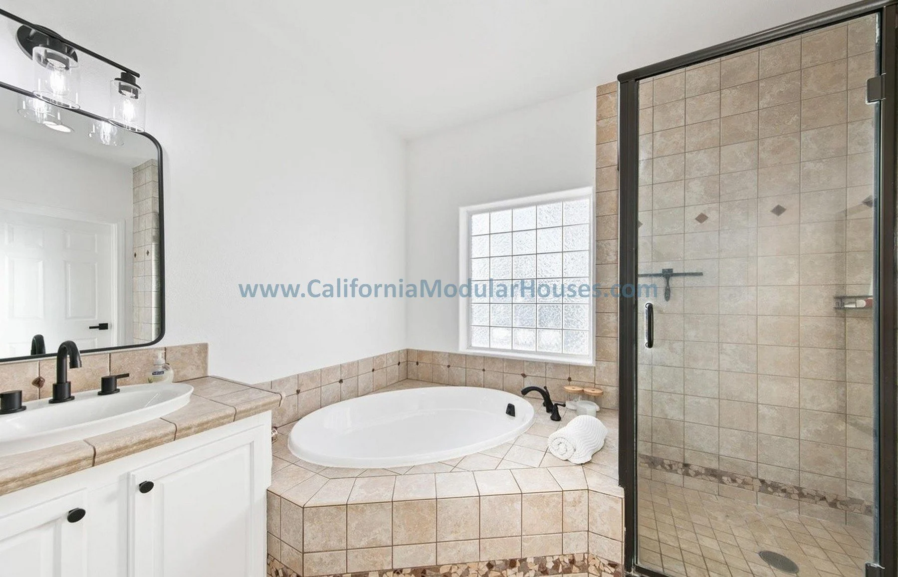 Bathroom with a bathtub, glass shower, vanity with sink, mirror, black fixtures, window, and beige tile accents.