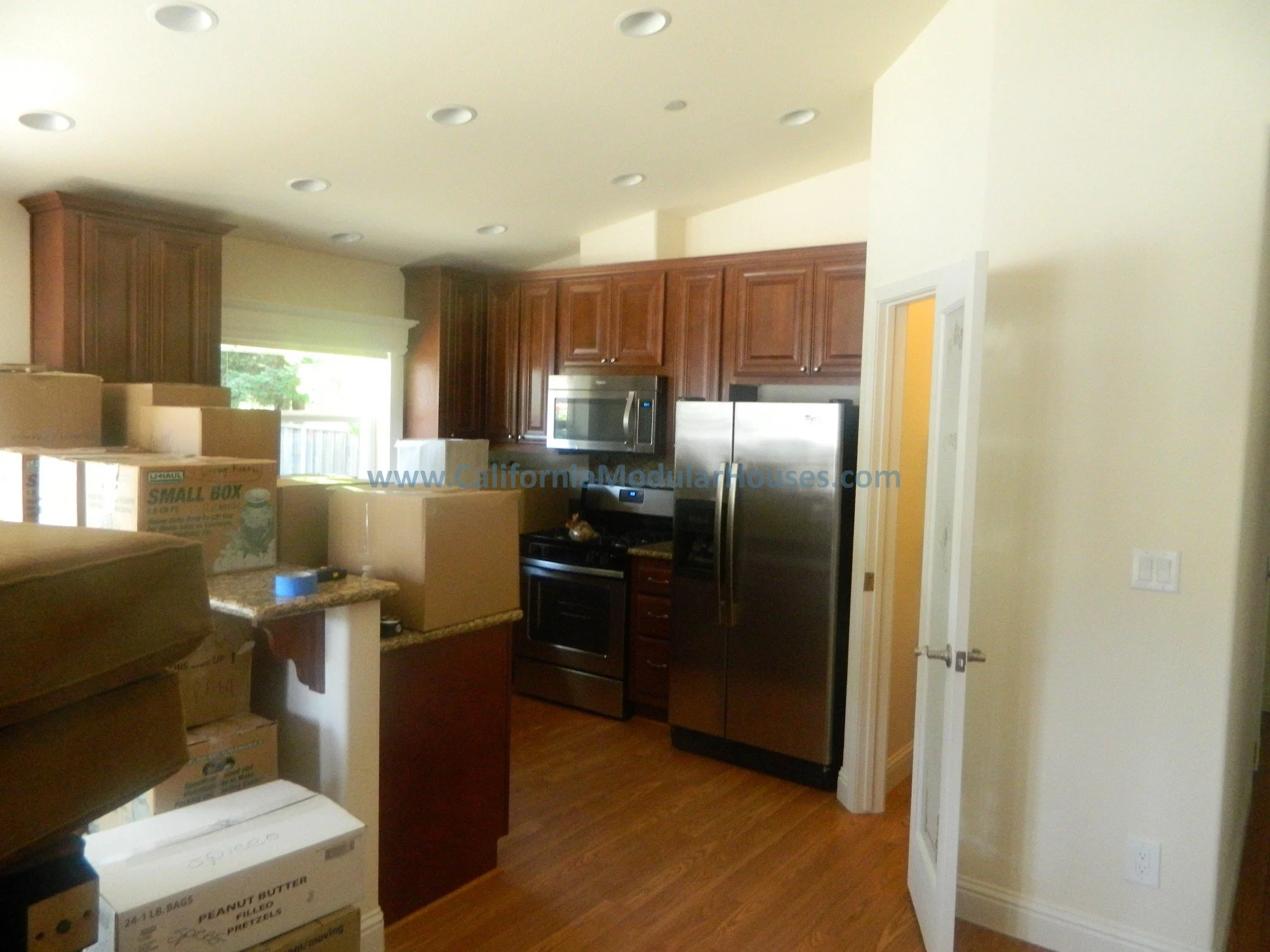 Kitchen with wooden cabinets, a stainless steel refrigerator, a microwave, and a stove, cluttered with moving boxes and packing supplies.