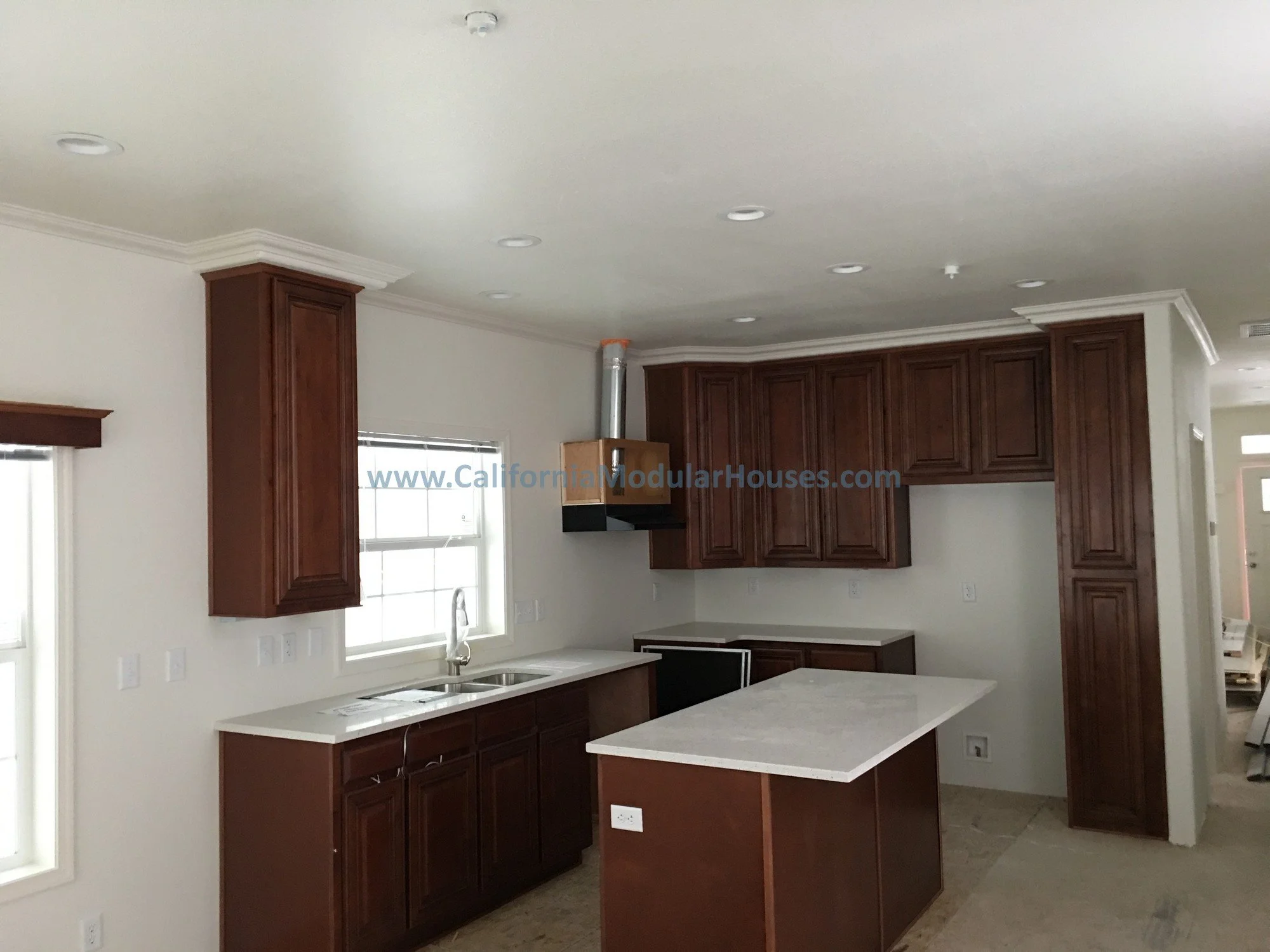 Empty kitchen with dark wooden cabinets, white countertops, a small island, and a window above the sink.