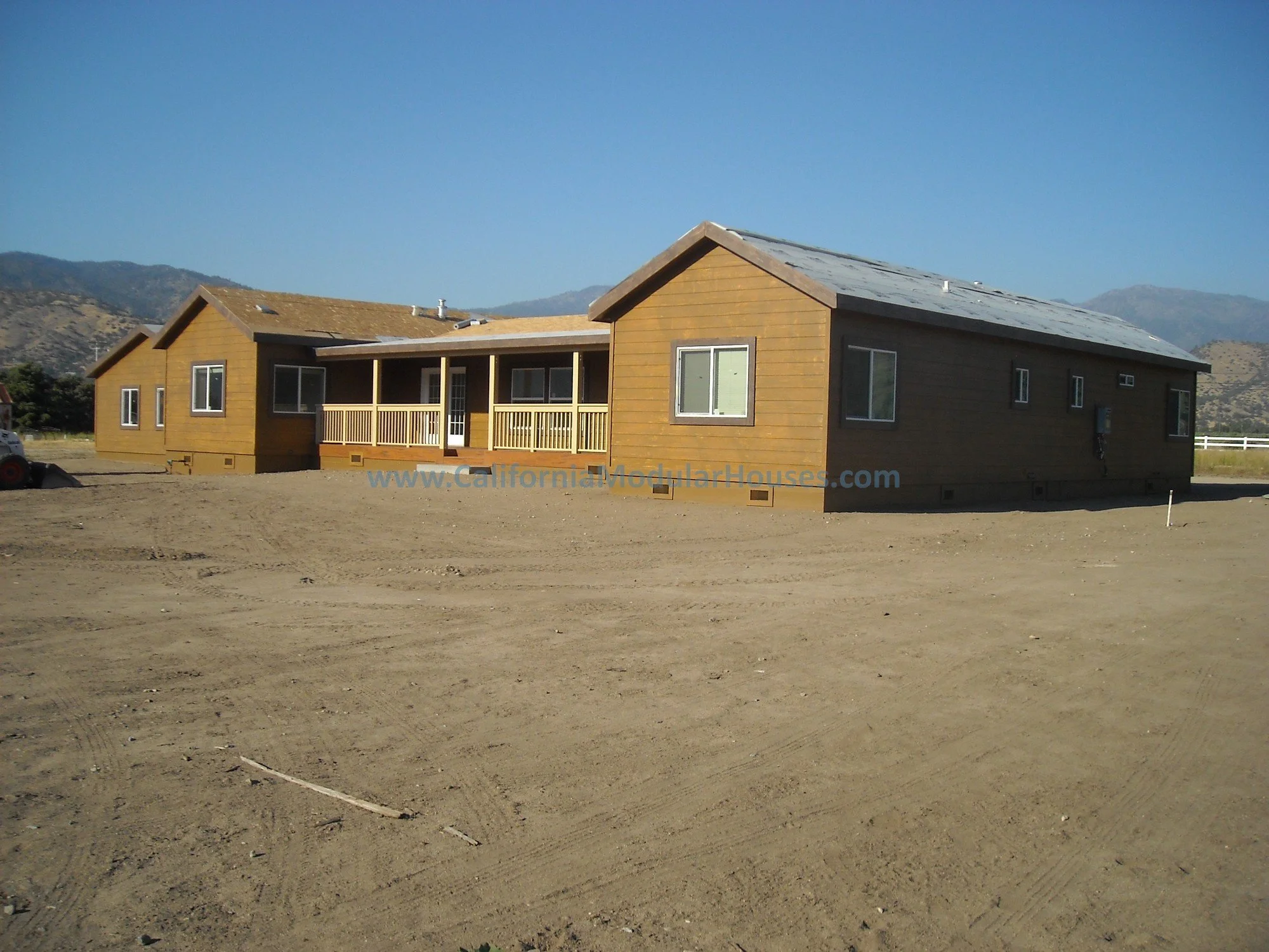 A new, unfinished wooden house on a dirt lot with mountains in the background.  This is a modular home in Kern County.  It is in a flood plain area and with the raised foundation it worked out perfectly.  Custom designed by our team for this client. 