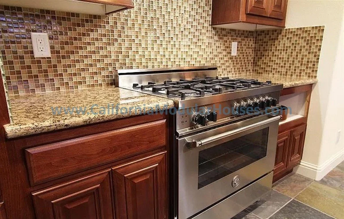 Stainless steel gas oven and stove with a granite countertop and wooden cabinets in a kitchen.