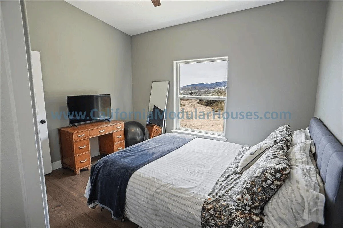 A bedroom with a bed, a wooden dresser with a TV on it, a mirror, a window showing a rural landscape, and an exercise ball on the floor.