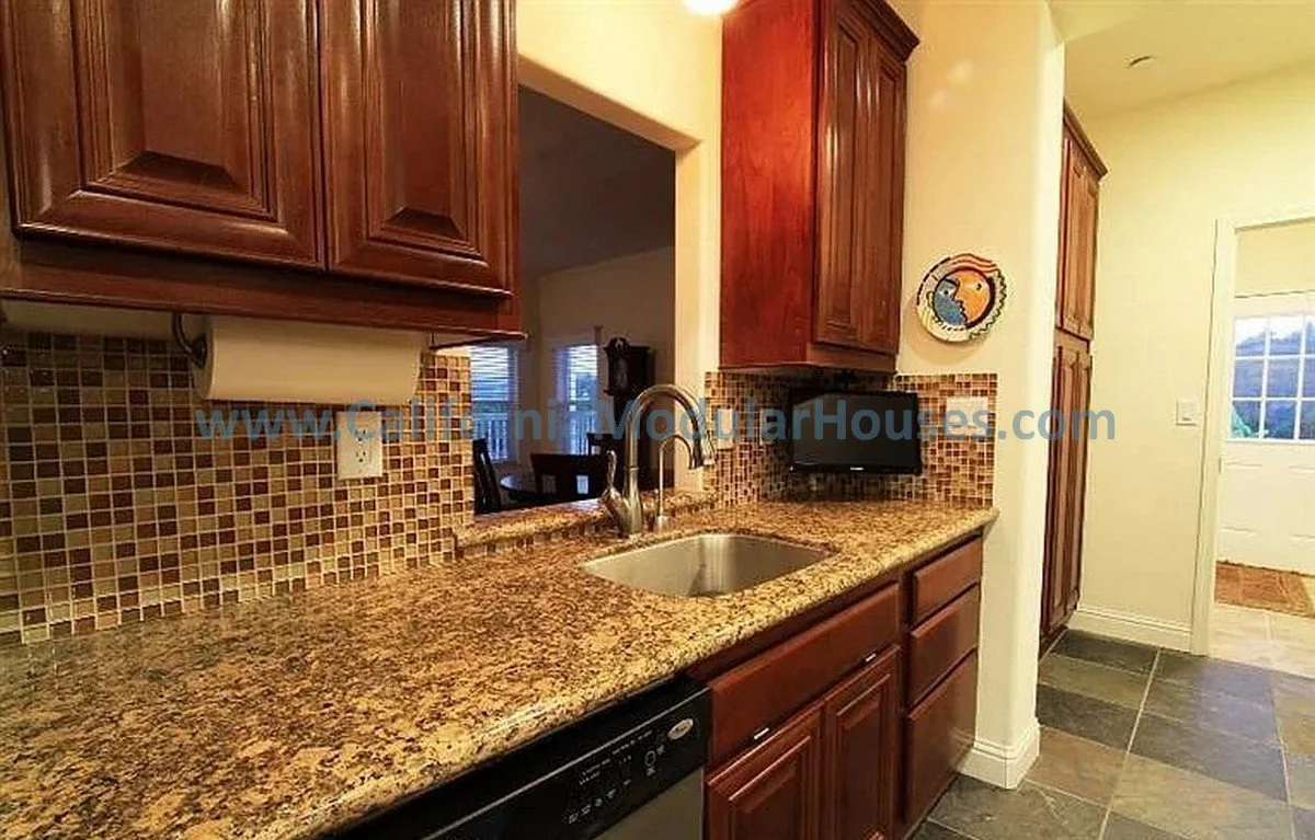 Kitchen with wooden cabinets, granite countertop, mosaic tile backsplash, small TV, and sink with a faucet.