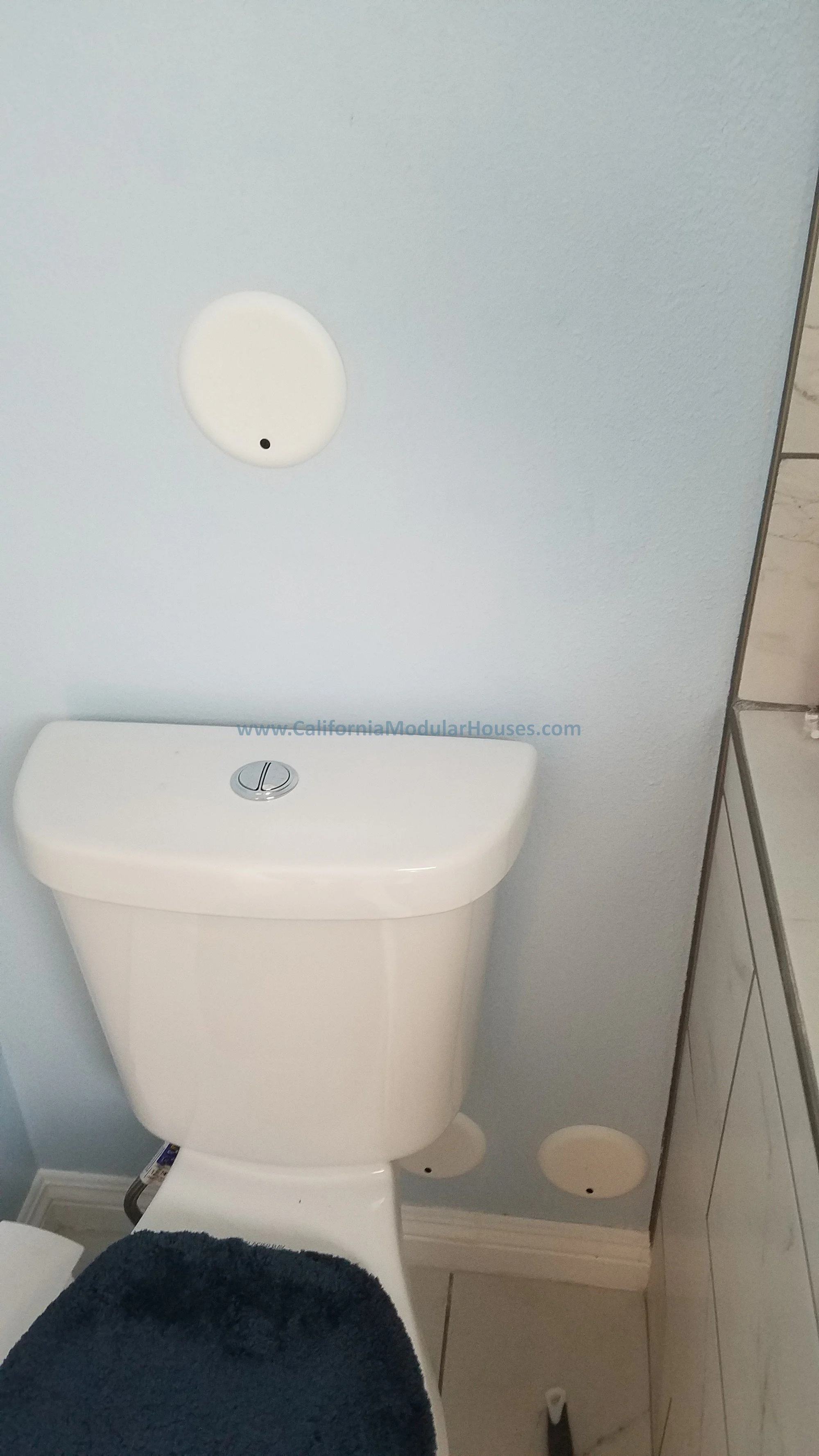 White toilet in a bathroom with round vents on the wall and a cabinet to the right.   Modular.  