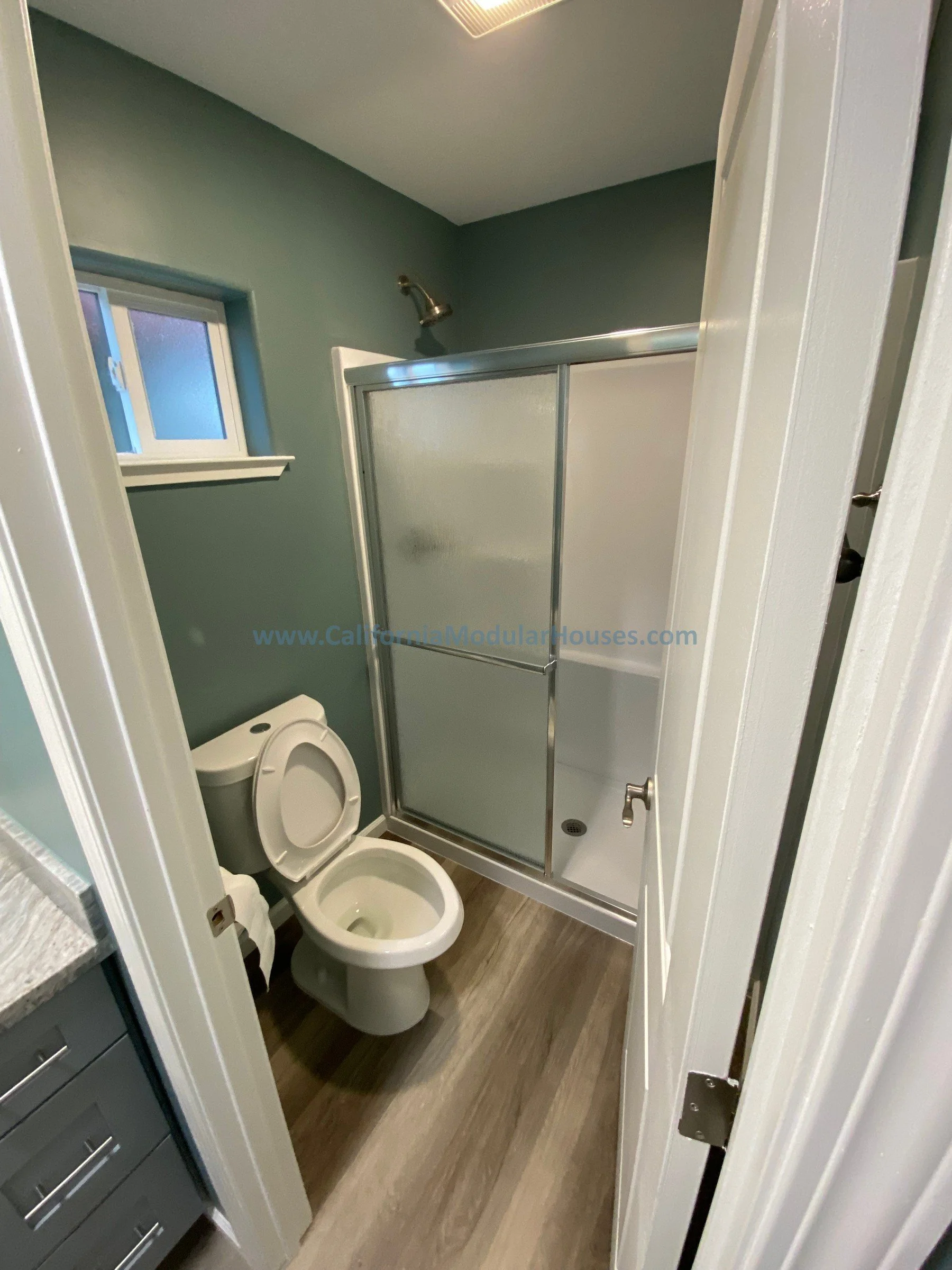 The bathroom interior with toilet, small window, and shower enclosed with frosted glass doors.  Modular ADU Modular Accessory Dwelling Unit