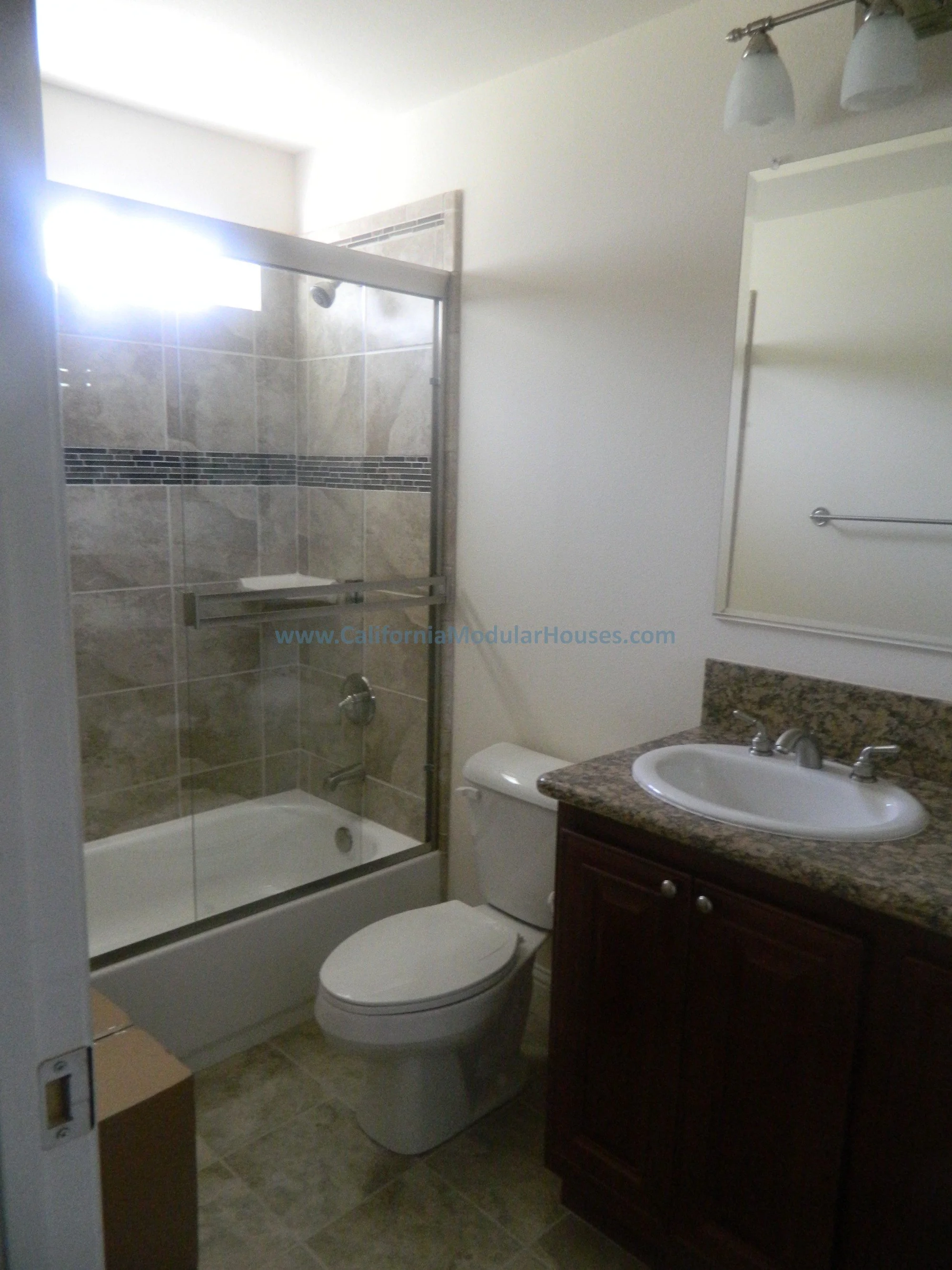 Bathroom with glass shower enclosure, toilet, and vanity with granite countertop and sink.