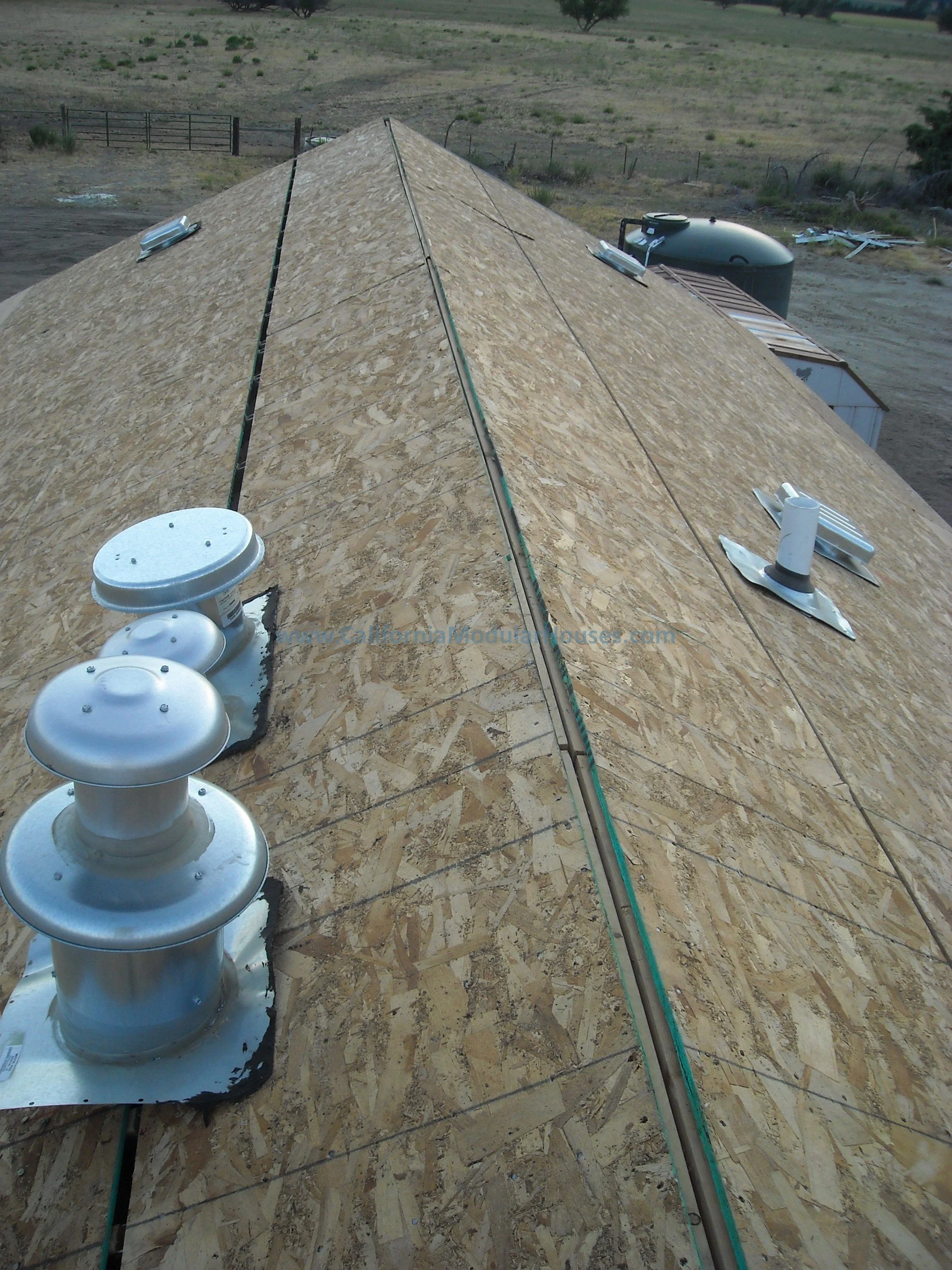 Close-up view of a new roof under construction, featuring an oriented strand board (OSB) roof deck with roofing vents installed.
