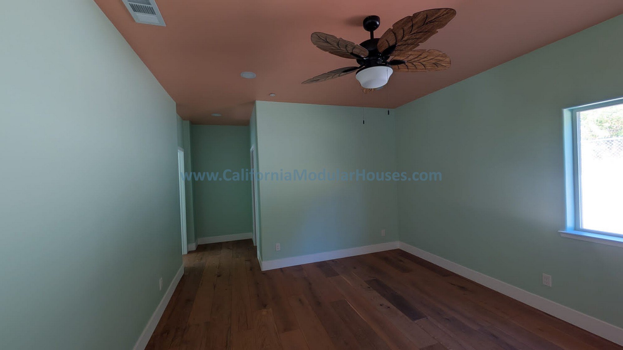 Empty room with mint green walls, hardwood floors, a ceiling fan with leaf-shaped blades, and a window on the right side.