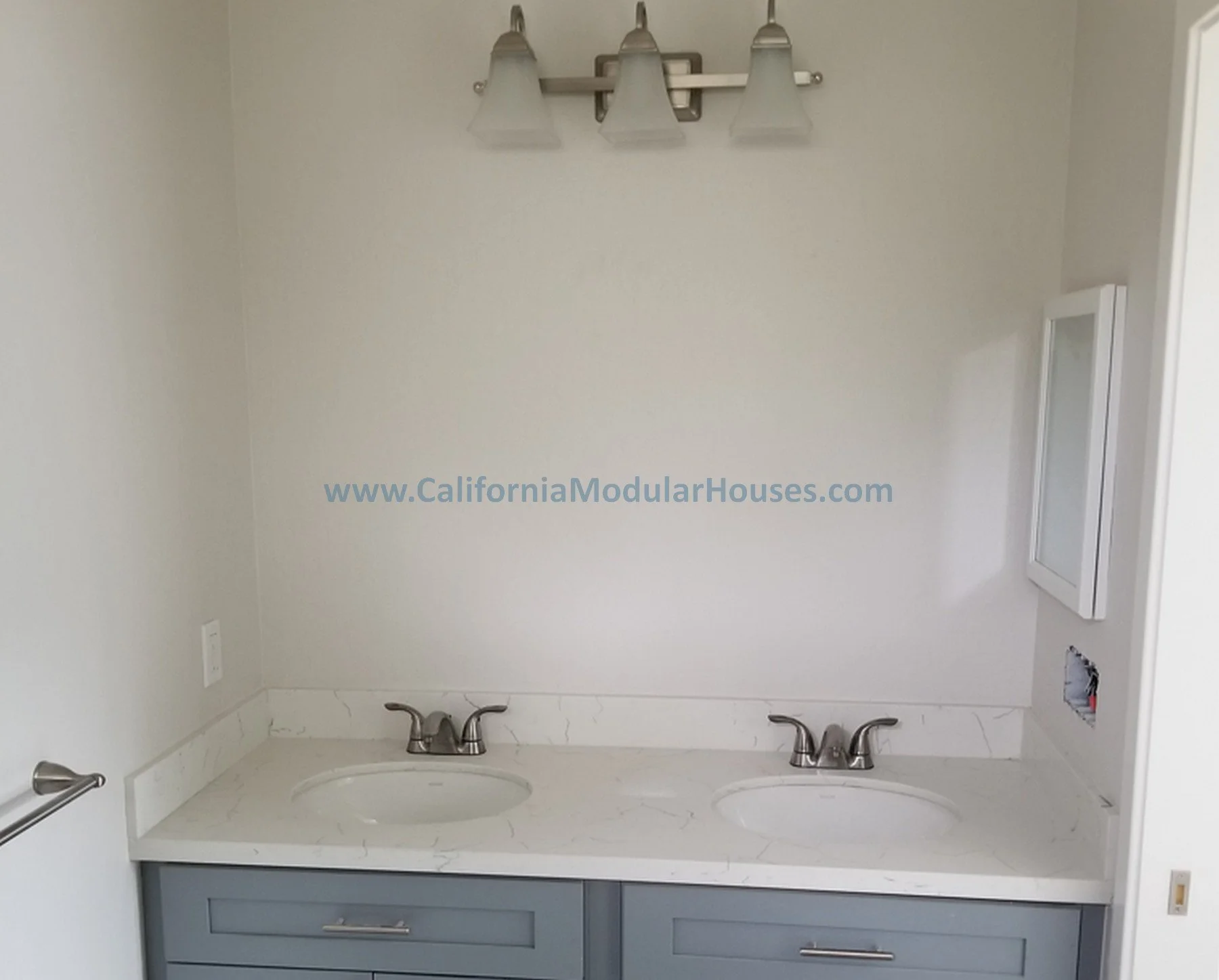 Bathroom with double sink vanity, wall-mounted mirror cabinet, and three-light fixture above mirror.  Picture of Interior Modular Prefab ADU.   California Modular Houses, Inc.