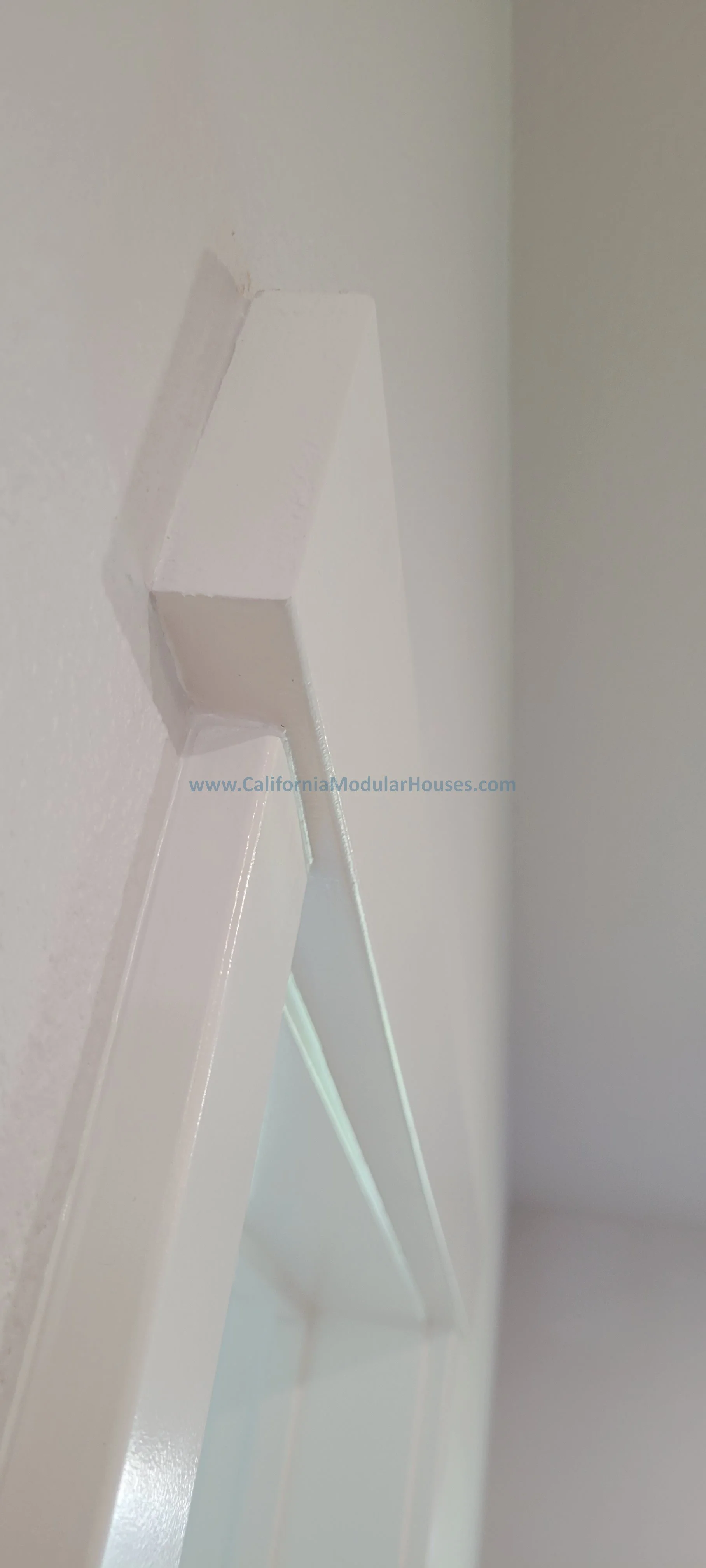 Close-up of a white, partially assembled modular wall unit or shelf with interlocking pieces, installed on a wall painted in light neutral color.