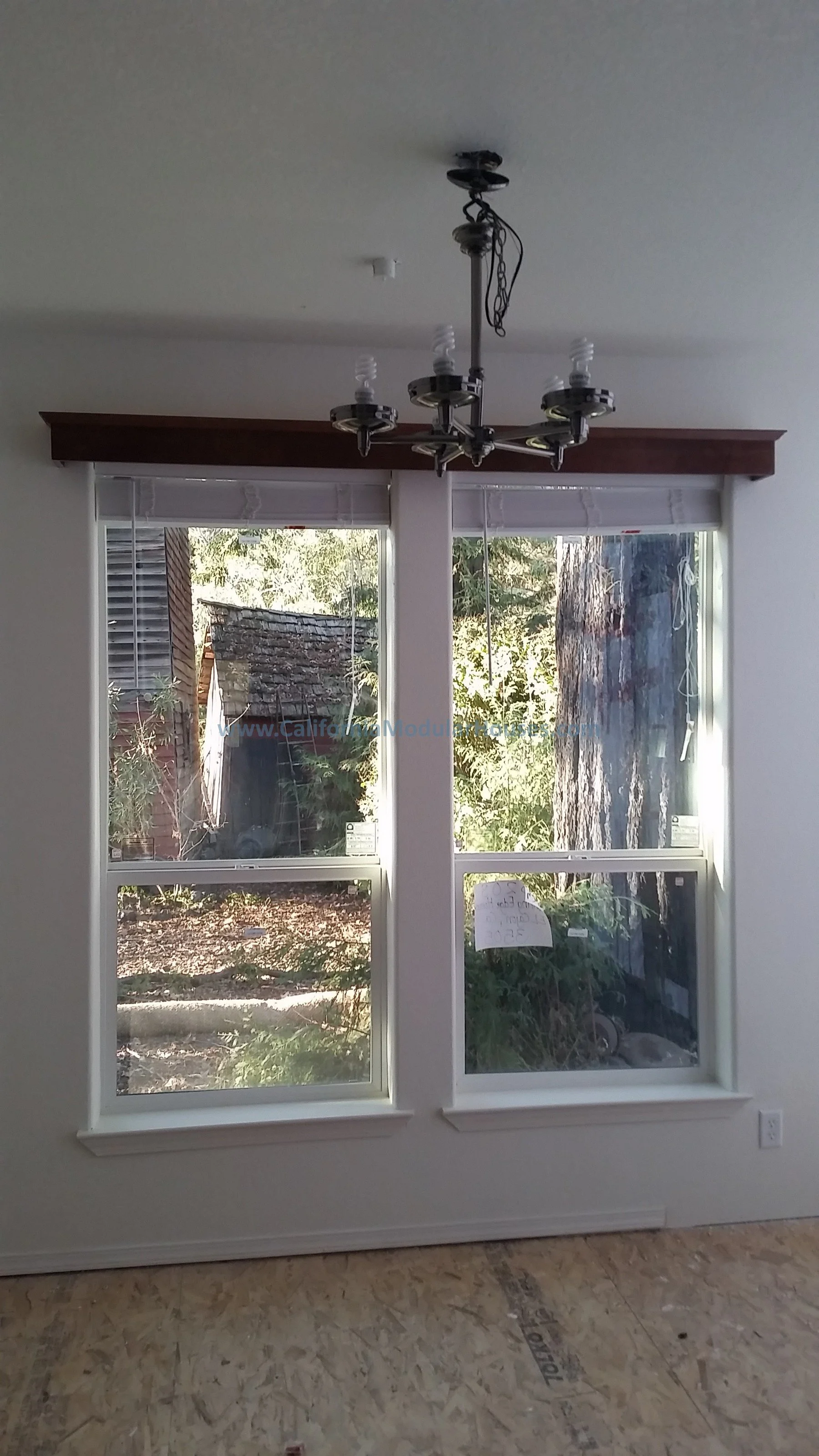 Empty room with two windows, a ceiling light fixture, and unfinished plywood flooring.  Interior Modular Prefab ADU Photograph  Morgan Hill, Santa Clara County, CA 