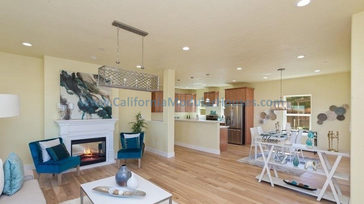 Open-concept living and dining room with fireplace, blue chairs, artwork, and a kitchen with stainless steel appliances.  California modular home.  prefab modular CA