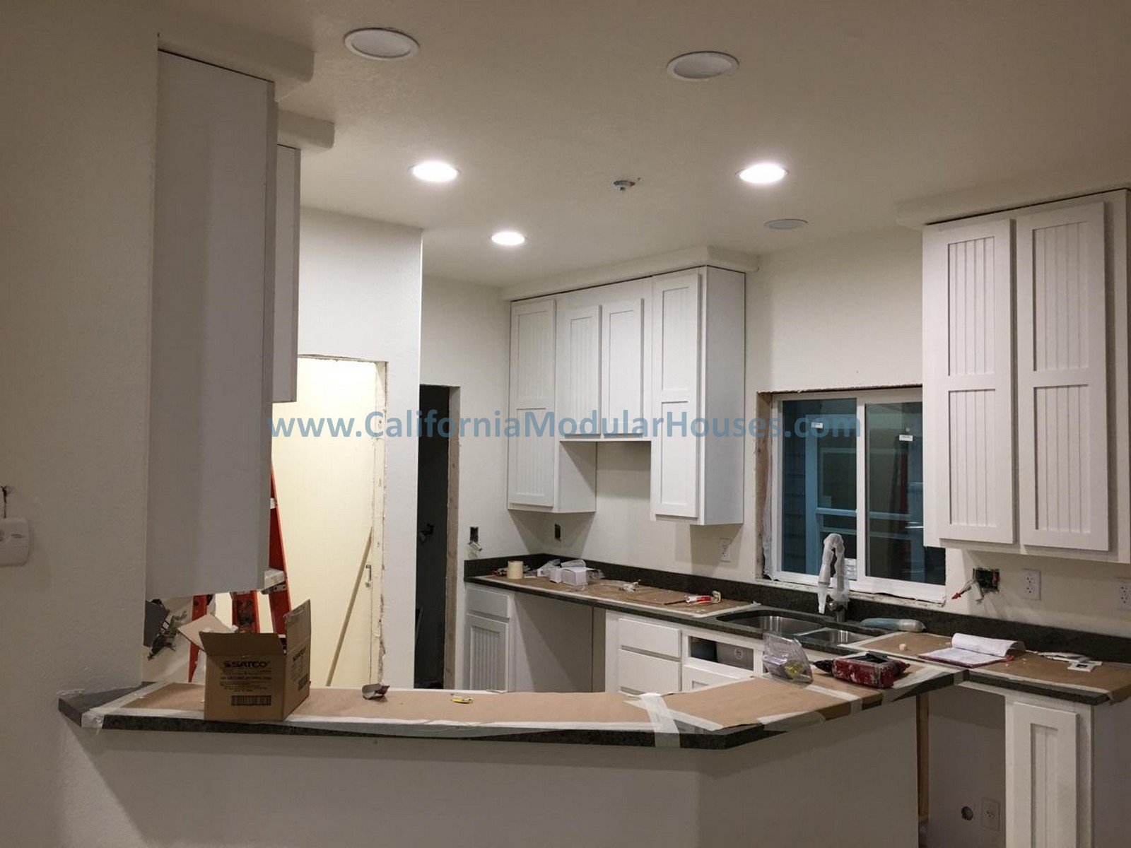 Kitchen under construction with white cabinets, black quartz countertops, and a window over the sink, featuring construction tools and materials.  New Home.  