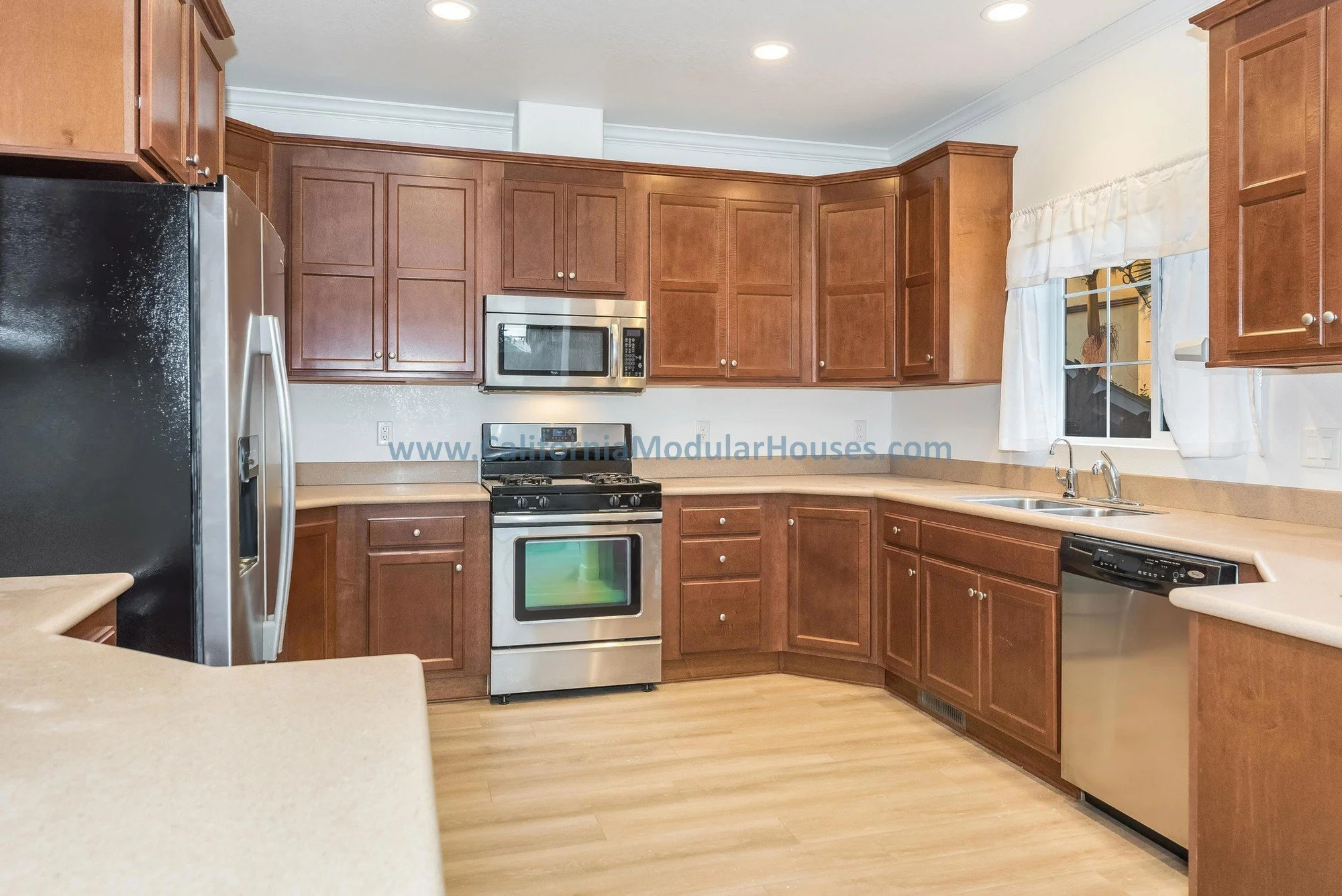 Cherry oak cabinets, white quartz countertop, stainless steel appliances of a kitchen of a prefab modular two-story home.