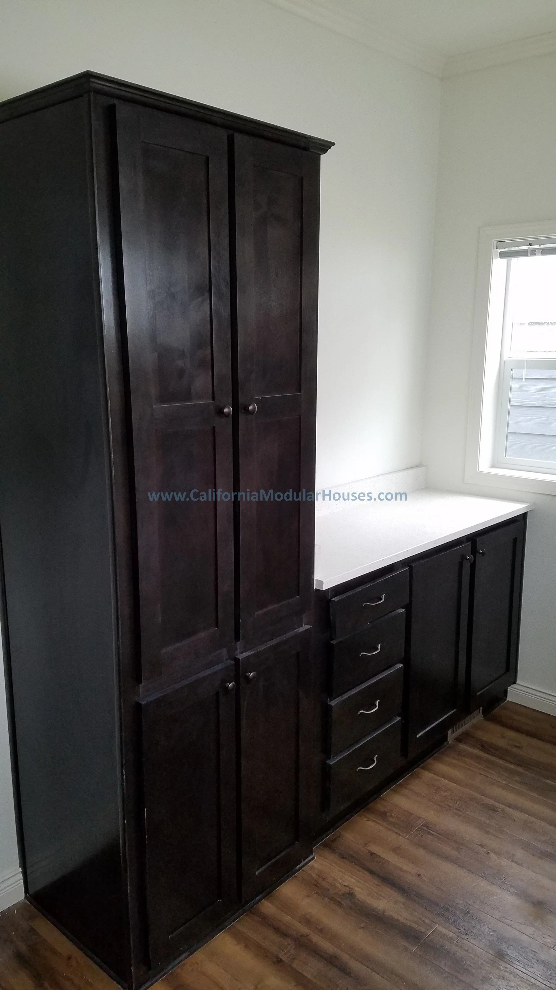 Dark wooden cabinet with multiple doors and drawers next to a window in a room with wood flooring. Two-Story Modular Home.Modular Home CA,
