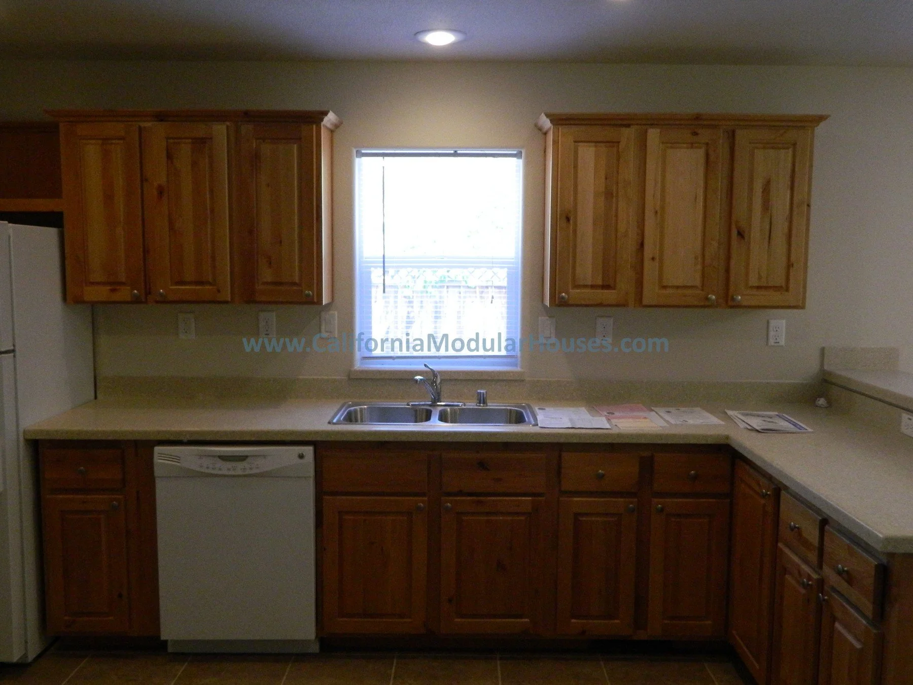 Kitchen with wooden cabinets, a window above a double sink, and a white dishwasher.