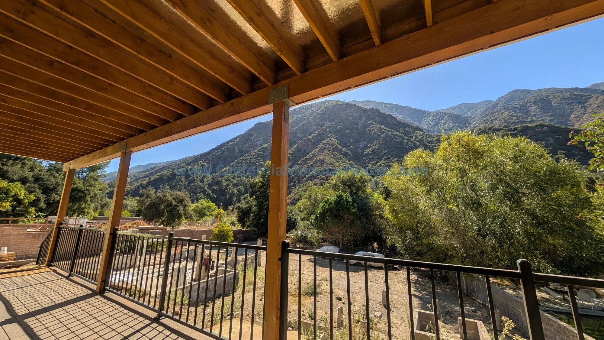 View from a balcony showing mountains, trees, and a dirt parking area with cars and structures in California.