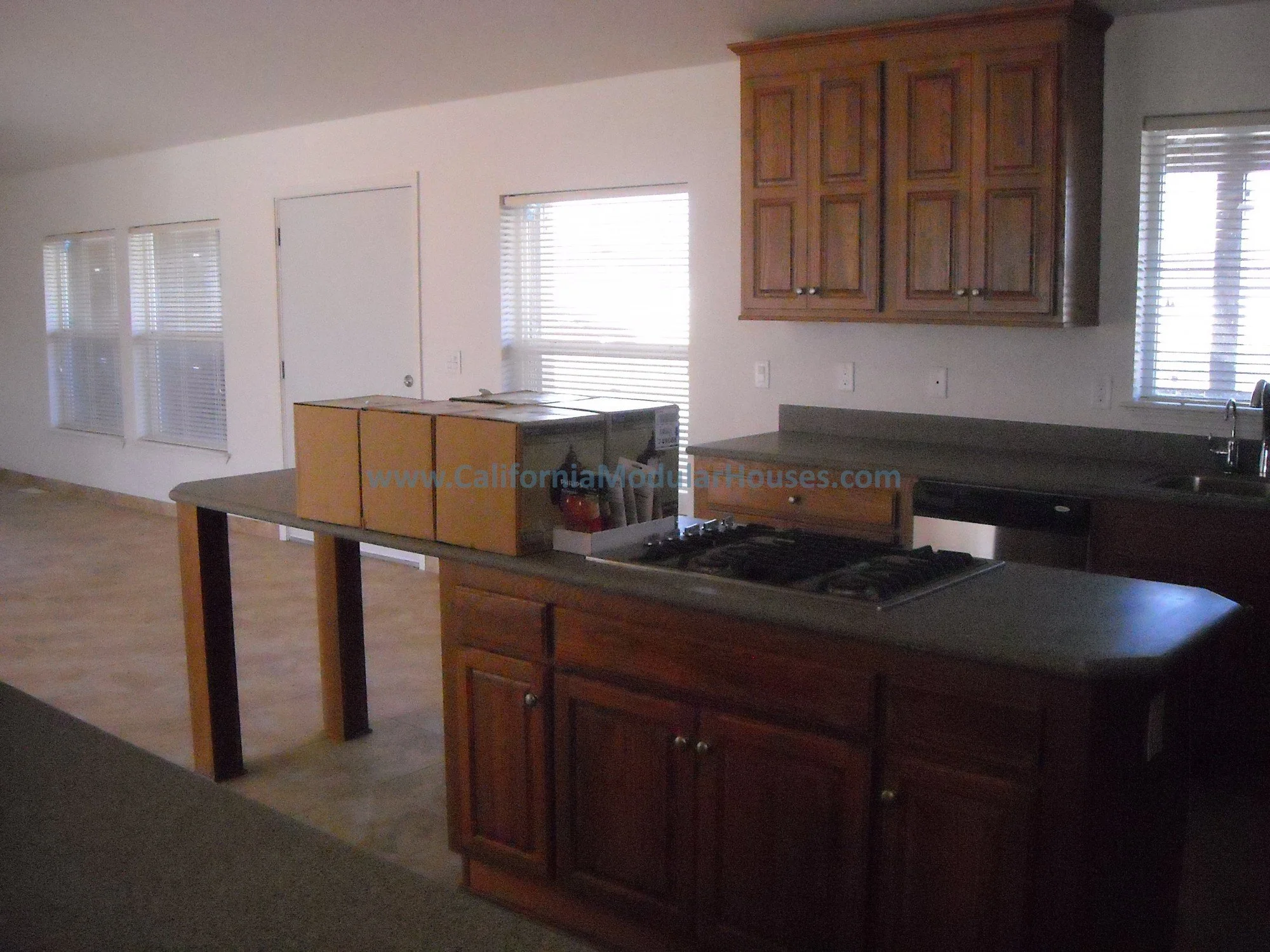 over-sized kitchen with dark wood cabinets, a stove, and large windows with blinds in a modern home with hard surface countertops and a huge center island.  