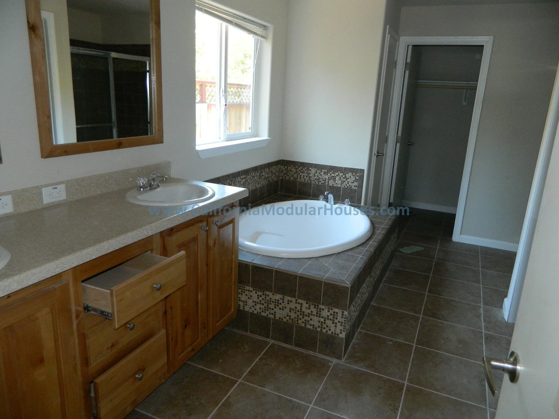 Bathroom with double vanity and mirror, large bathtub with mosaic tiles, open closet, and window