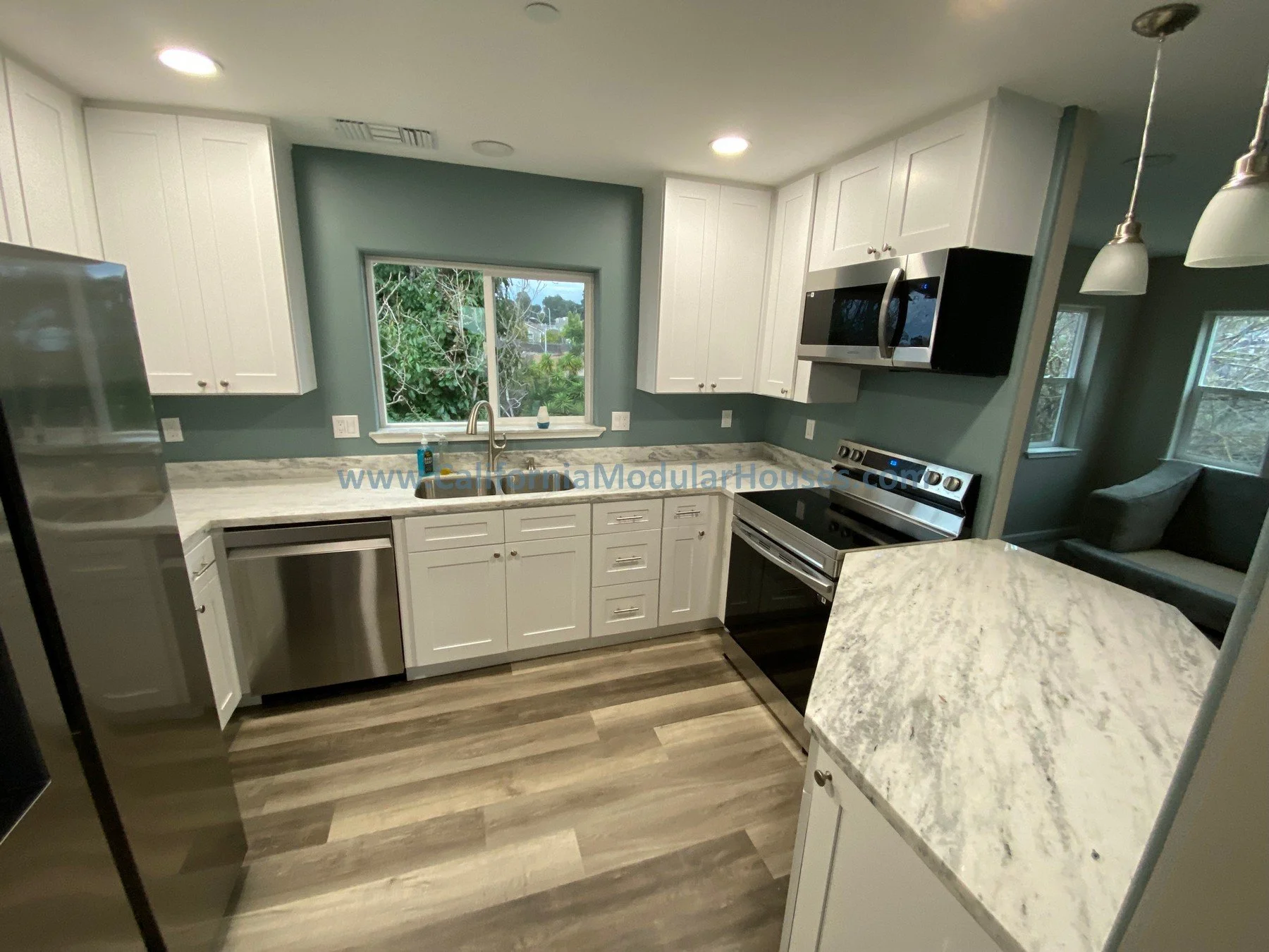 Modular Contra Costa County, CA.  Modern kitchen with white cabinets, marble countertops, and stainless steel appliances, including a refrigerator, dishwasher, microwave, and stove. A window above the sink