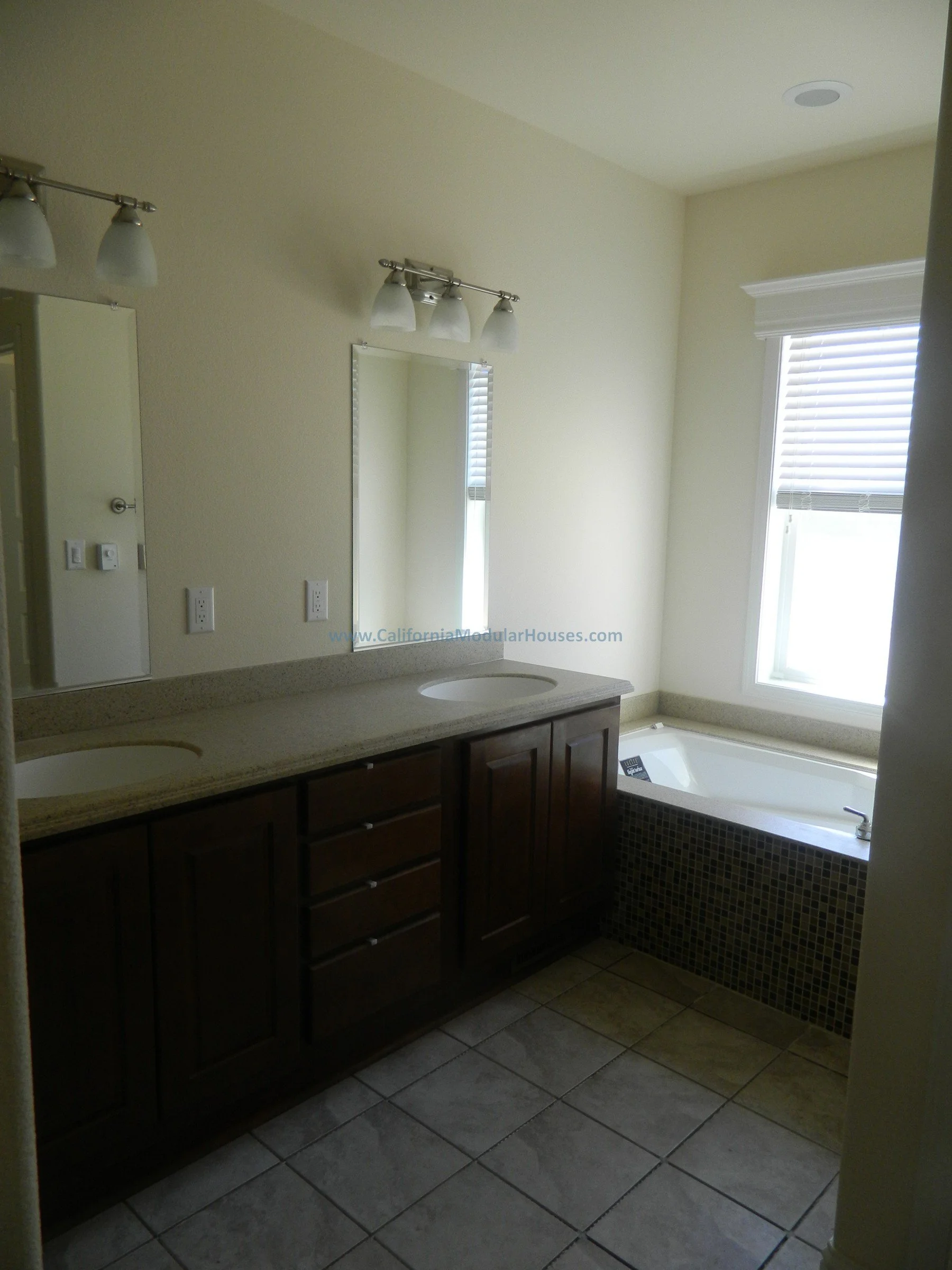 Bathroom with double sink vanity, mirror, window with blinds, and bathtub, beige walls, tiled floor, and modern light fixtures.  San Francisco Bay Area, CA.  Modular Homes Bay Area, Prefab Home California, Prefab Houses.