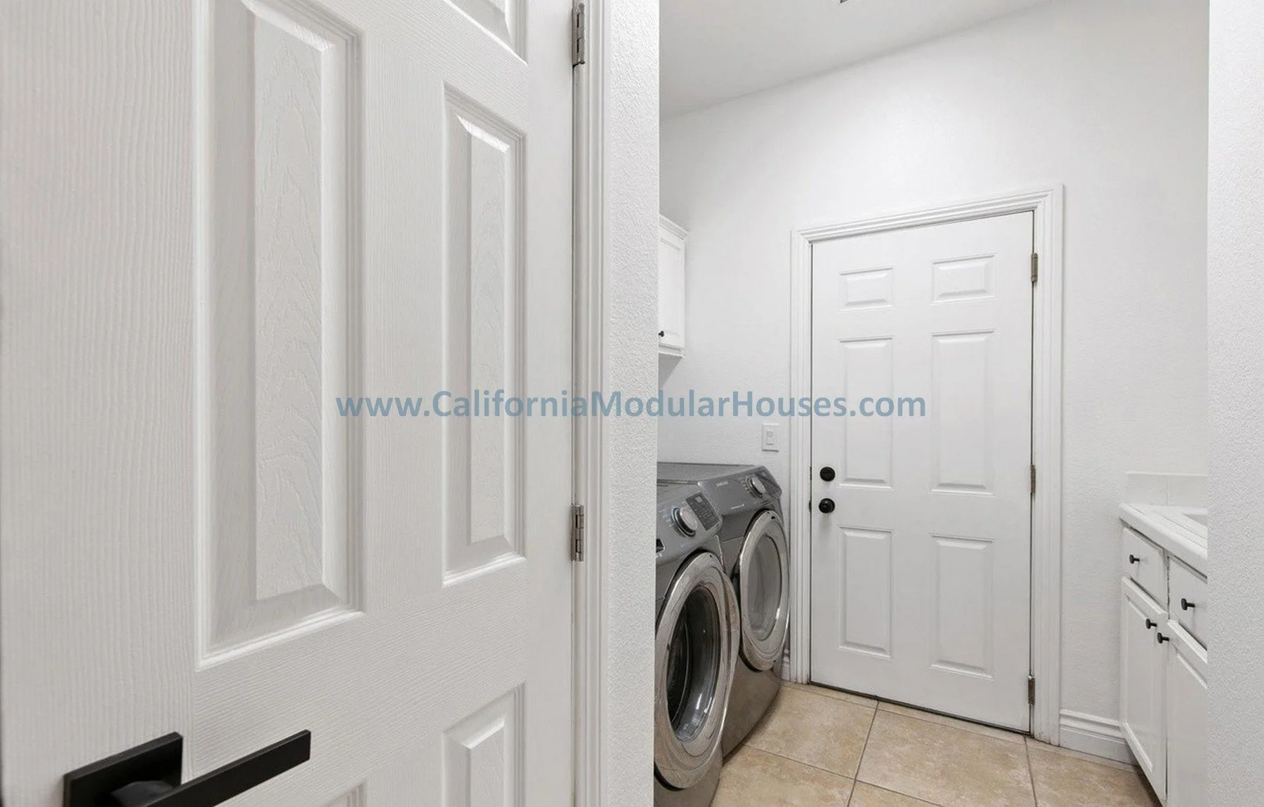 Laundry room with white walls, white doors, a washer and dryer, a countertop, and a white cabinet with black handles.