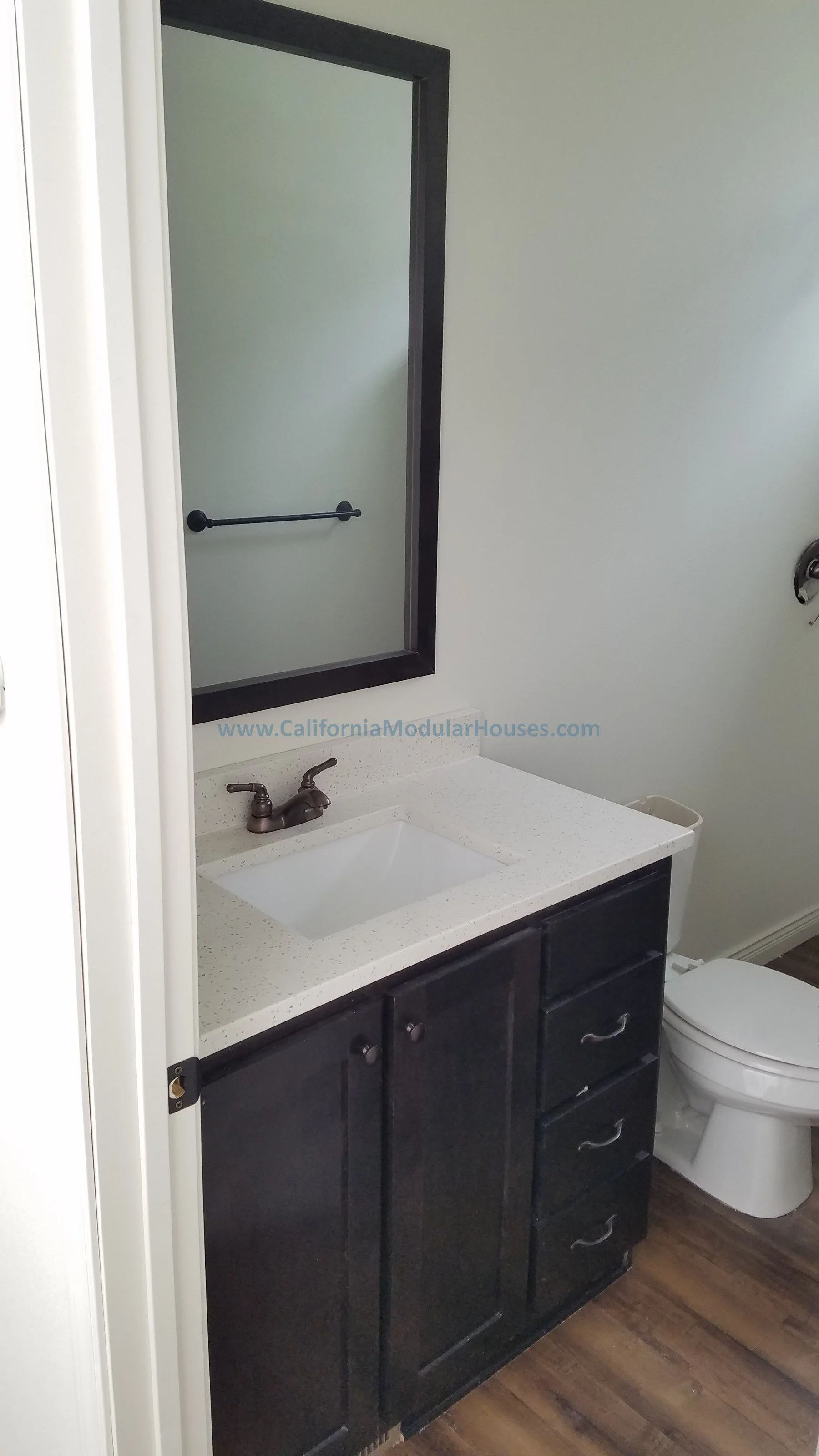 Bathroom with a mirror, sink, black cabinet, and toilet.  City of Santa Barbara, Santa Barbara County, CA.   Modular Home on a Sloped Property.  Pre-Fabricated Homes, Two-Story Modular Home.