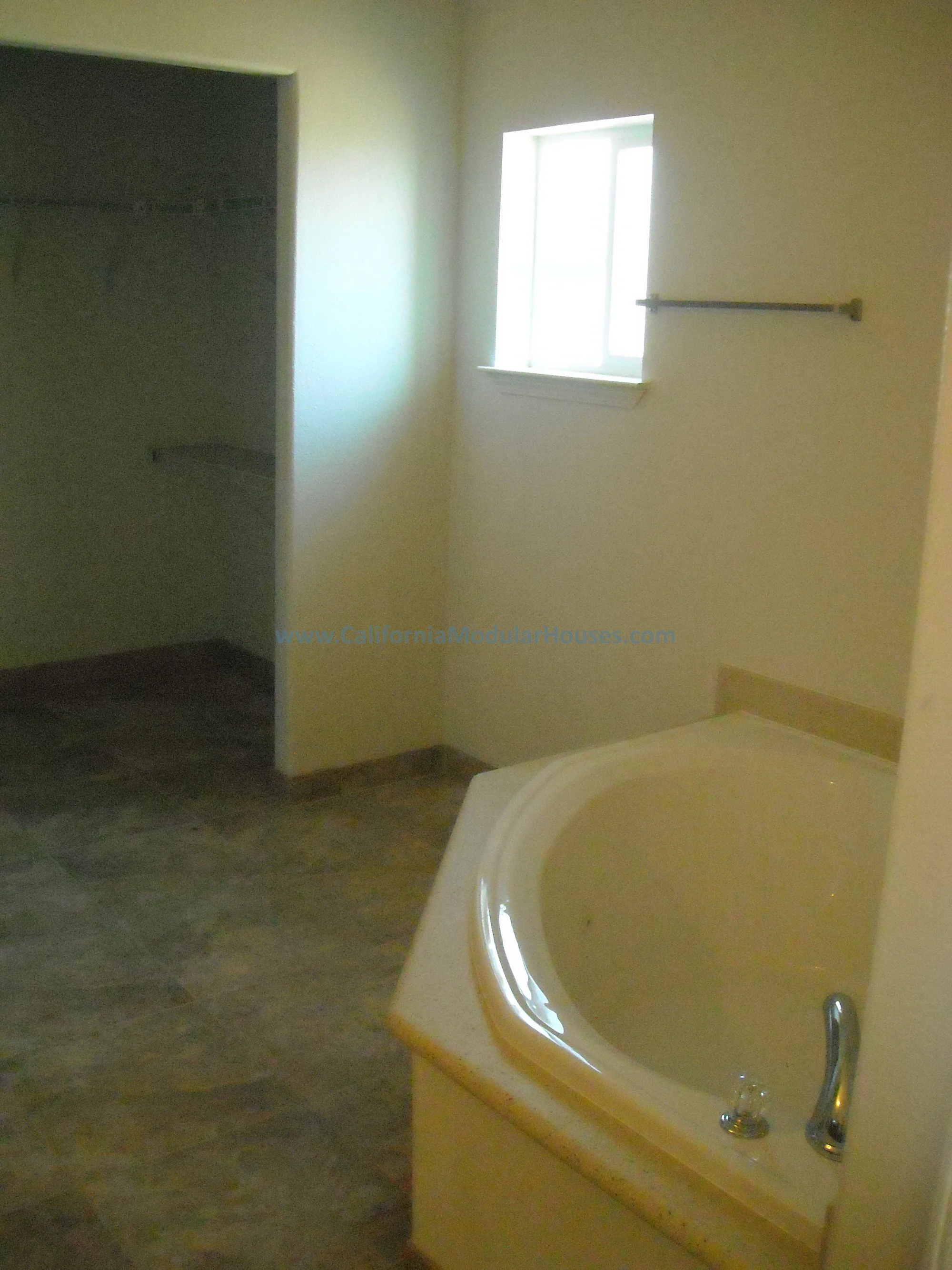 Empty bathroom with a corner soaking bathtub, a nicely placed window, and and a large walk-in closet for all of your clothes.  Factory Built Housing.  