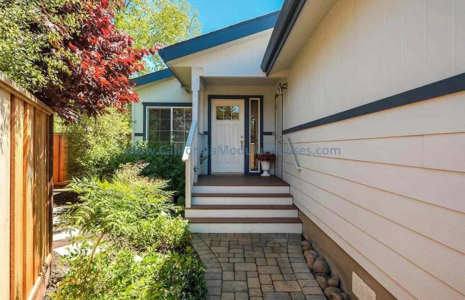 White prefab modular house with blue trim, front steps, potted plant, and a small porch light.