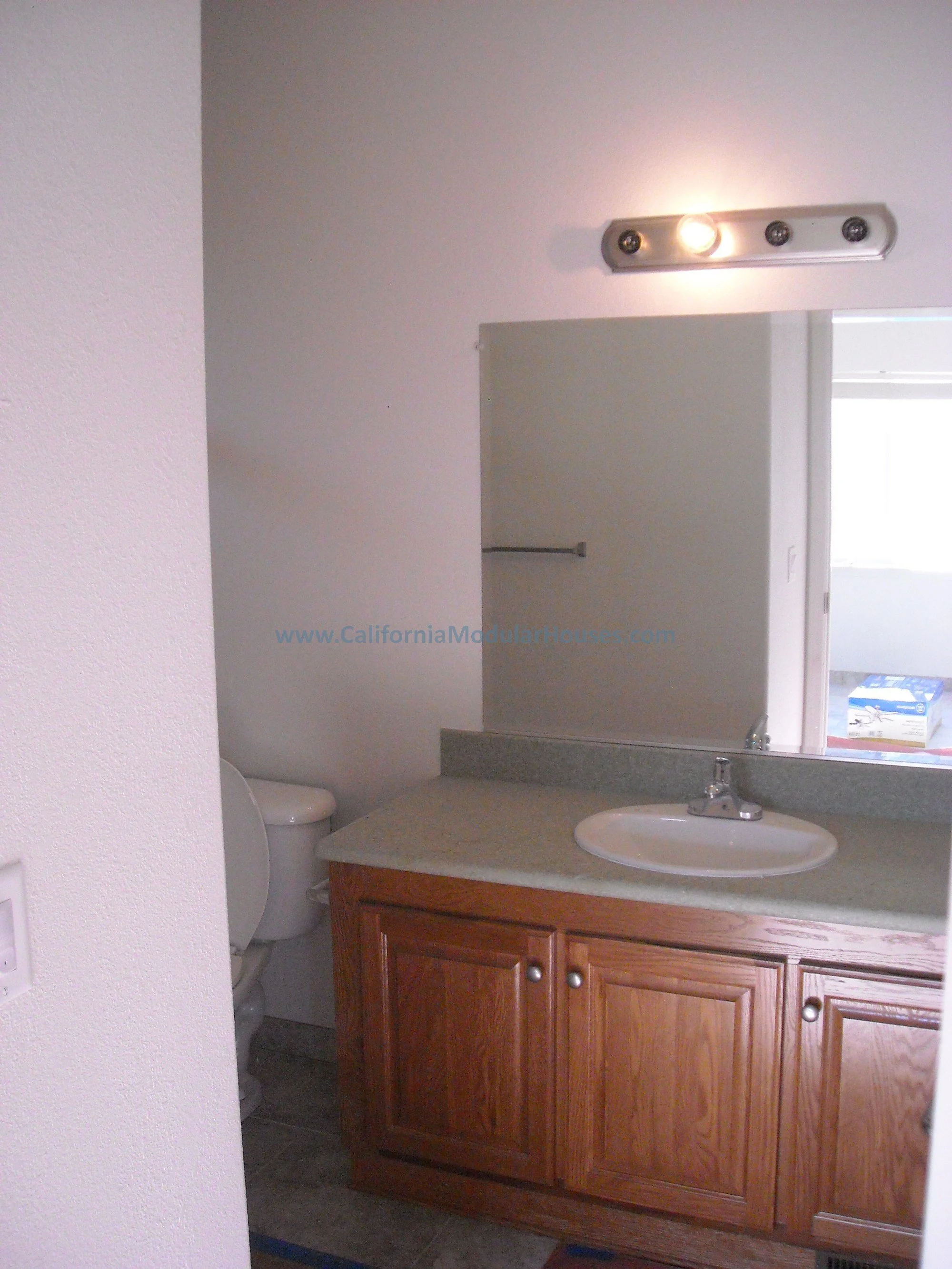 Bathroom with wooden vanity, hard surface countertop, sink, large mirror, toilet, and walls.  Modular Home for Central California Valley.  