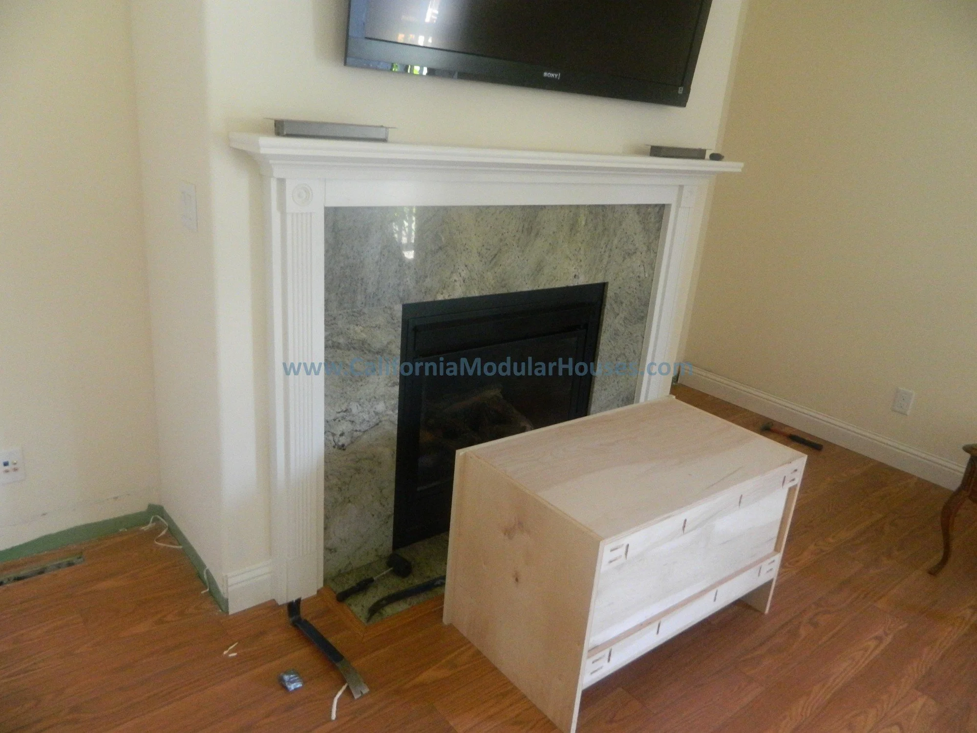 Living room with fireplace under a wall-mounted television, a wooden chest in front, and hardwood flooring.