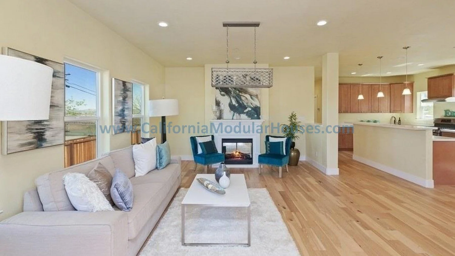Living room with beige sofa, blue chairs, fireplace, artwork, wooden floors, and open kitchen with pendant lights.  Contra Costa County 2 story modular home.  Modular house. 