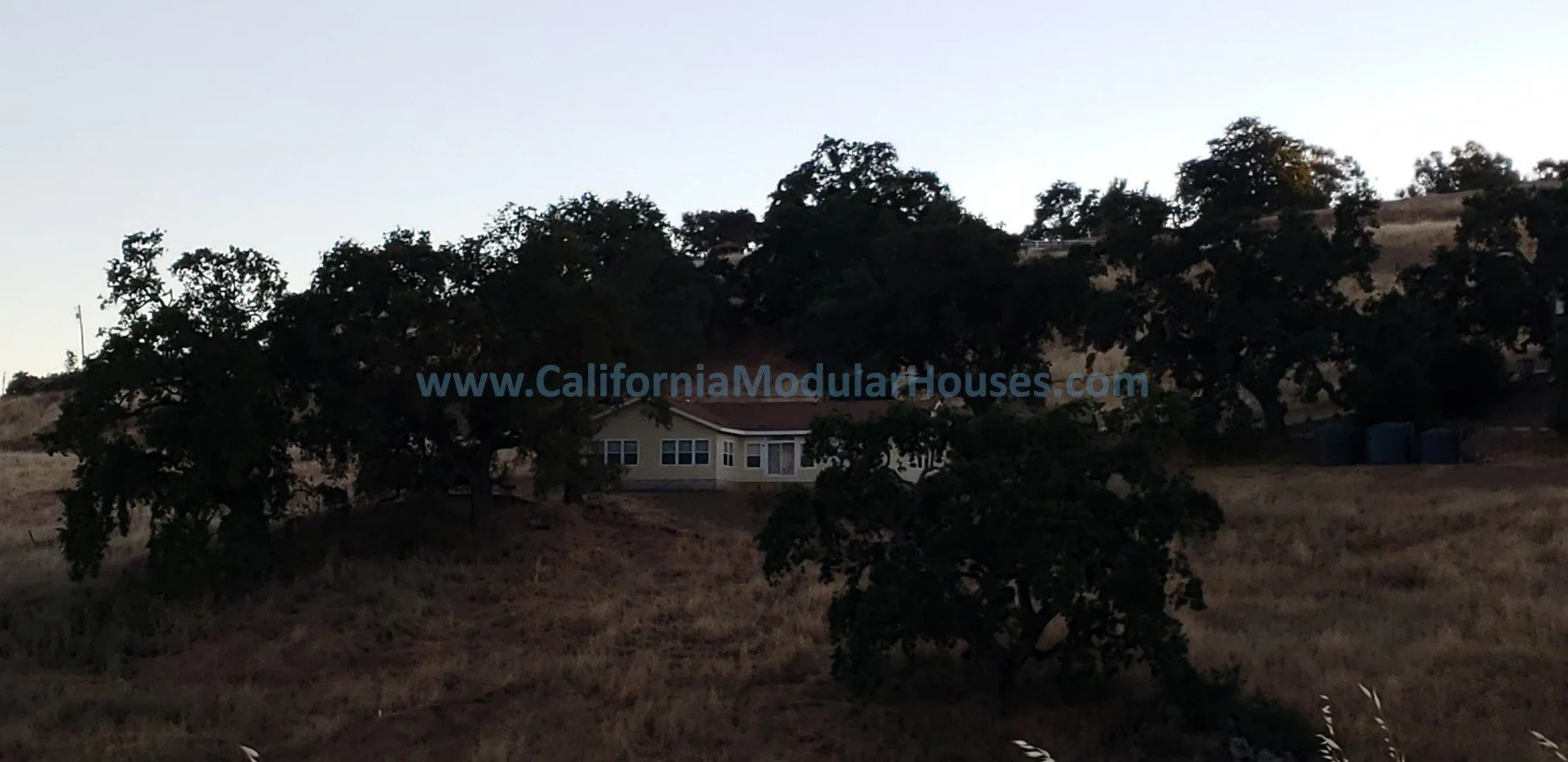A house on a hillside surrounded by trees, with a clear sky in the background. California Modular Houses,  Bay Area Prefab Modular Home, Pre-Fabricated Homes,