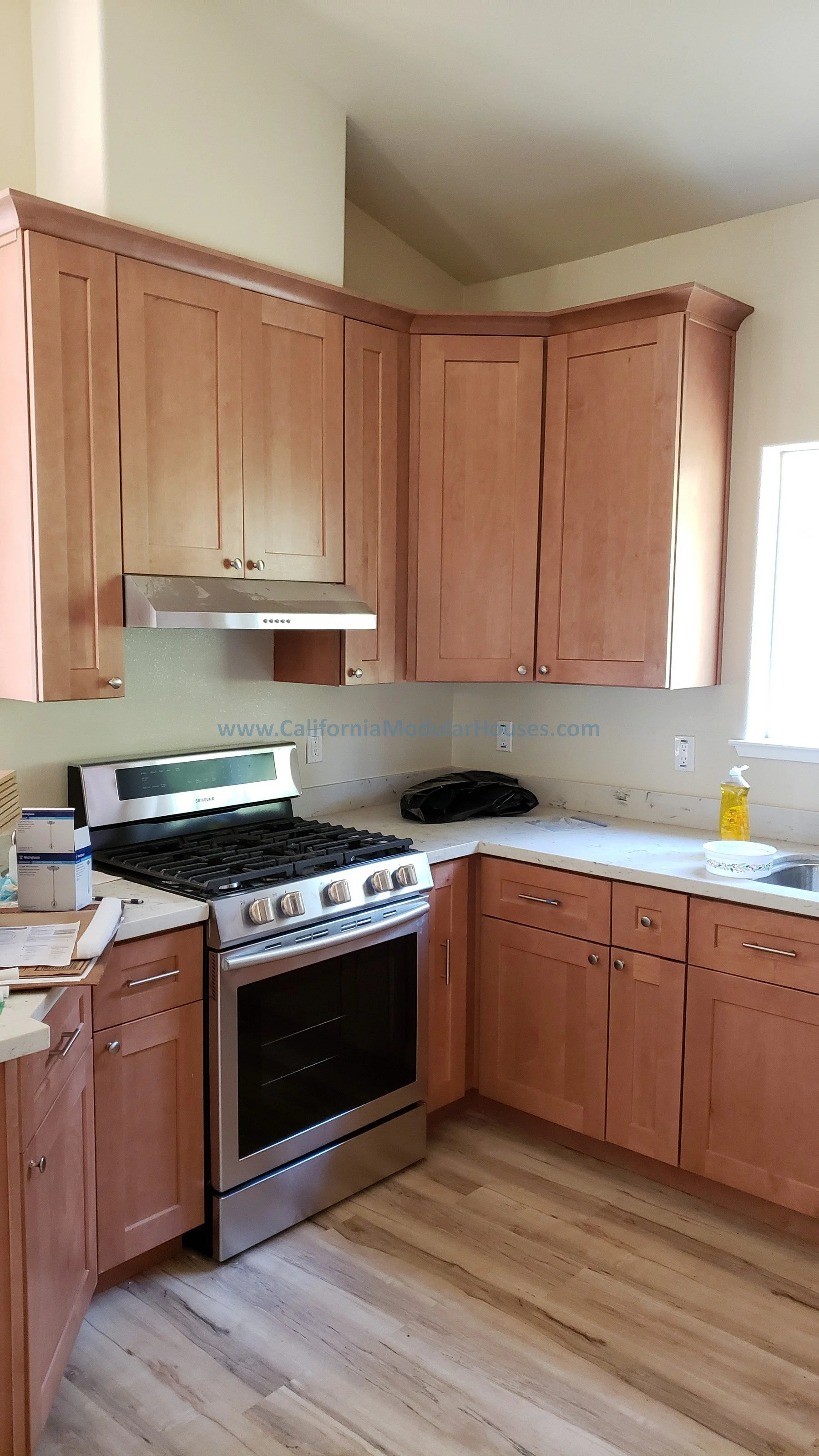 Kitchen with wooden cabinets, stainless steel stove, marble countertops, and a window with sunlight.  Prefab Modular ADU  Modular granny flat.  California.   