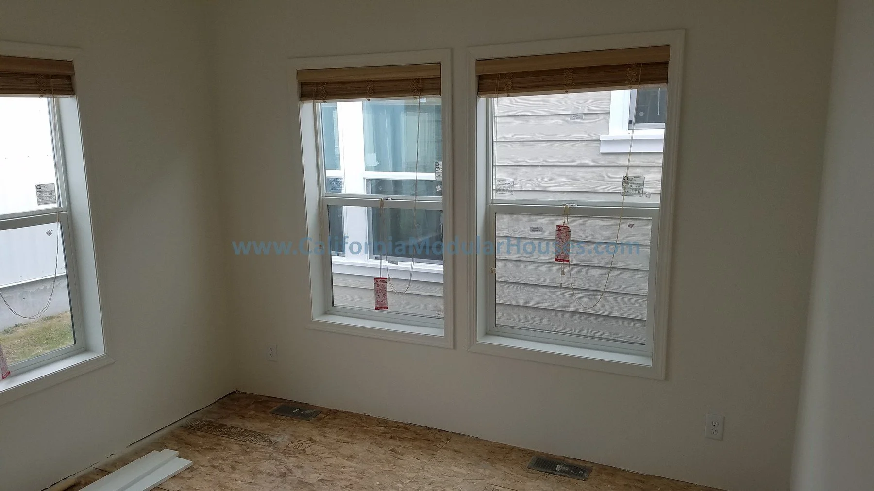 Empty room with large windows and wooden blinds, construction materials on the floor, and wall outlets visible.  City of Santa Barbara, Santa Barbara County, CA.  Modular Home on a Sloped Property. Modular Home CA,