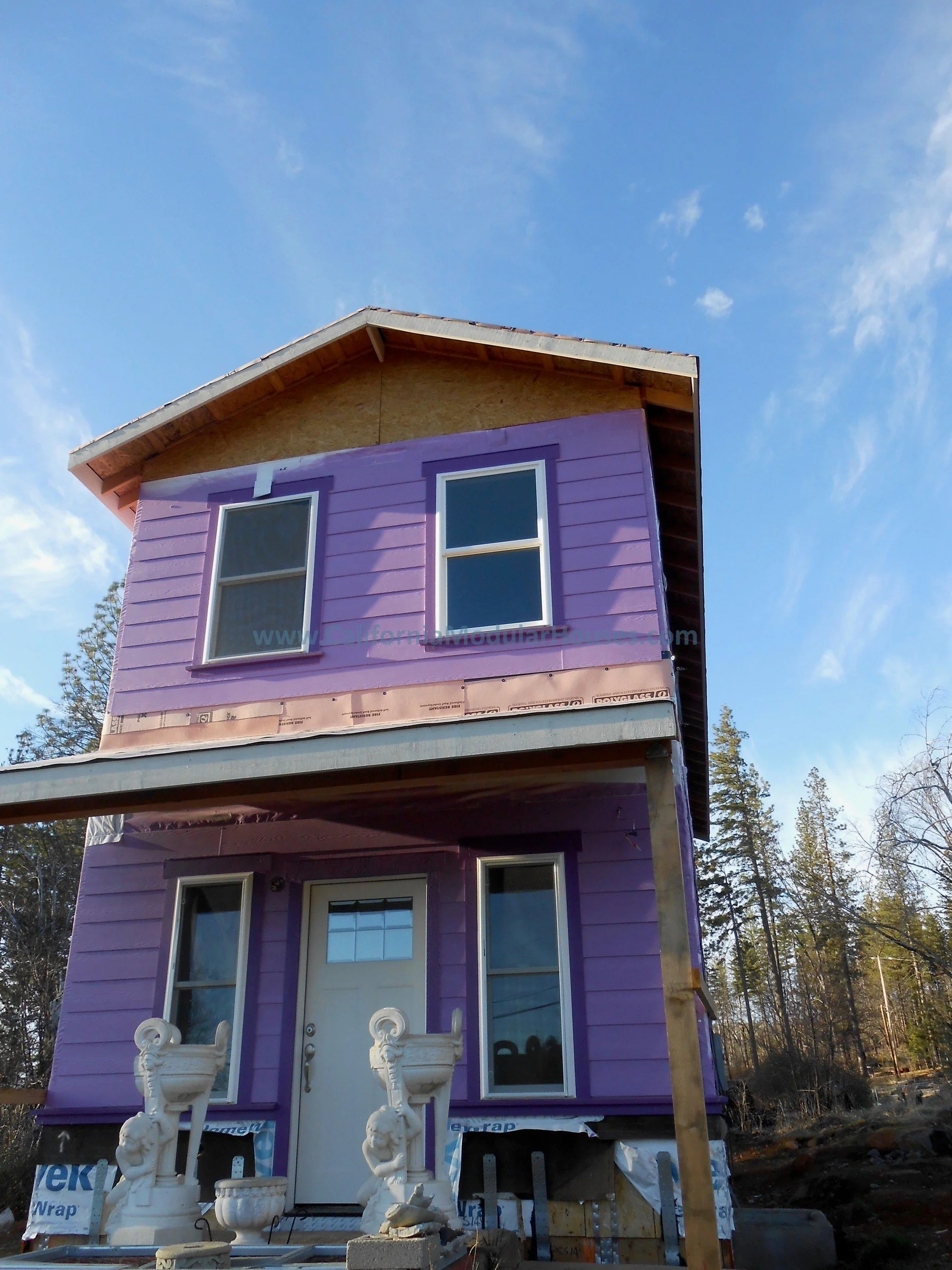 A two-story house under construction with purple siding, white door, and multiple windows. The house has a gabled roof.  Modular Home CA, California Modular Homes, Prefab Modular Homes California, California Modular,