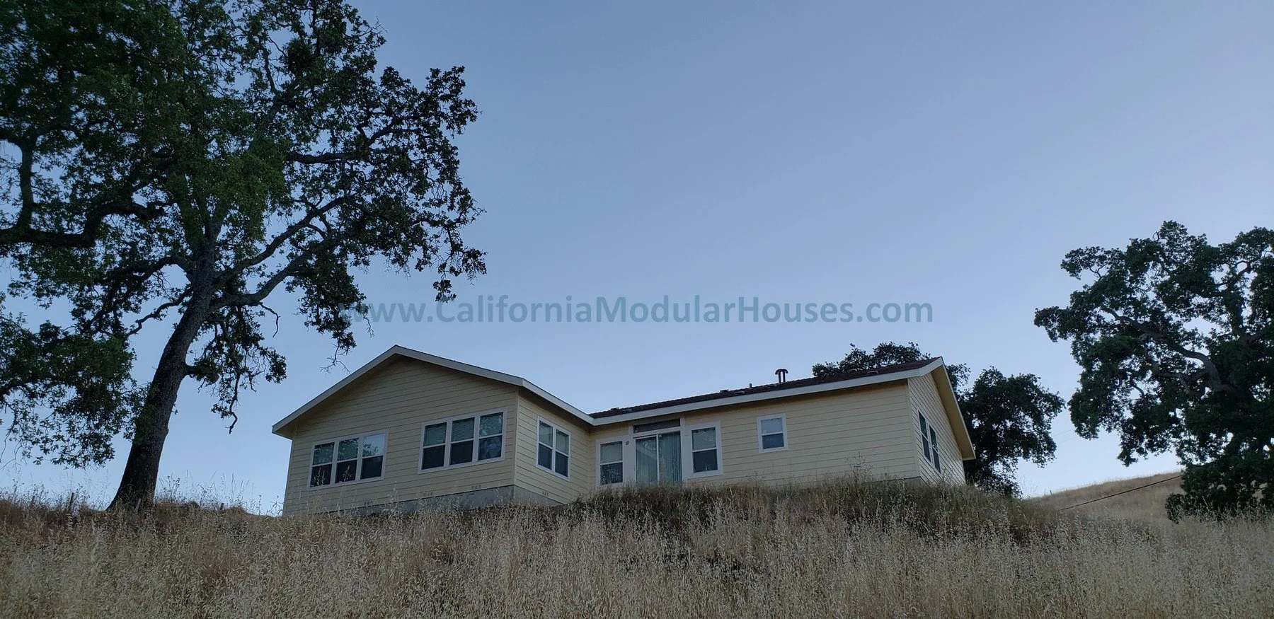 A house on a grassy hill with large trees on both sides and a clear evening sky in the background.  San Jose Prefab Homes, California Modular.