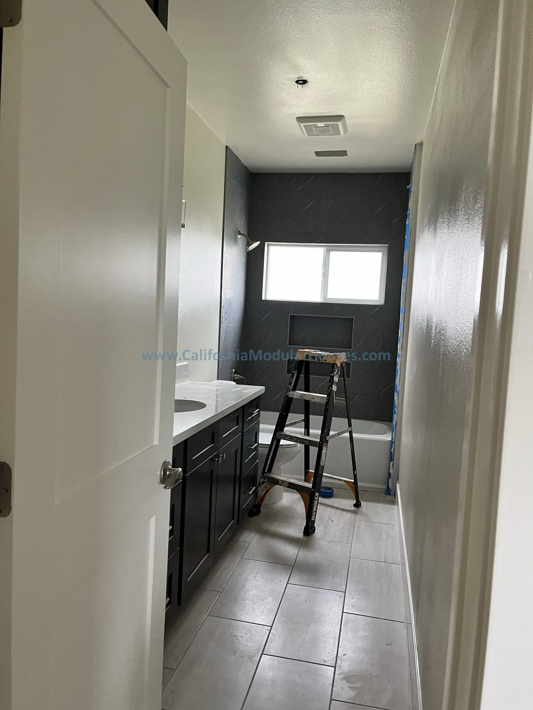 Interior view of a bathroom under renovation with a black vanity, a sink, a window, a bathtub, a ladder, and construction materials.